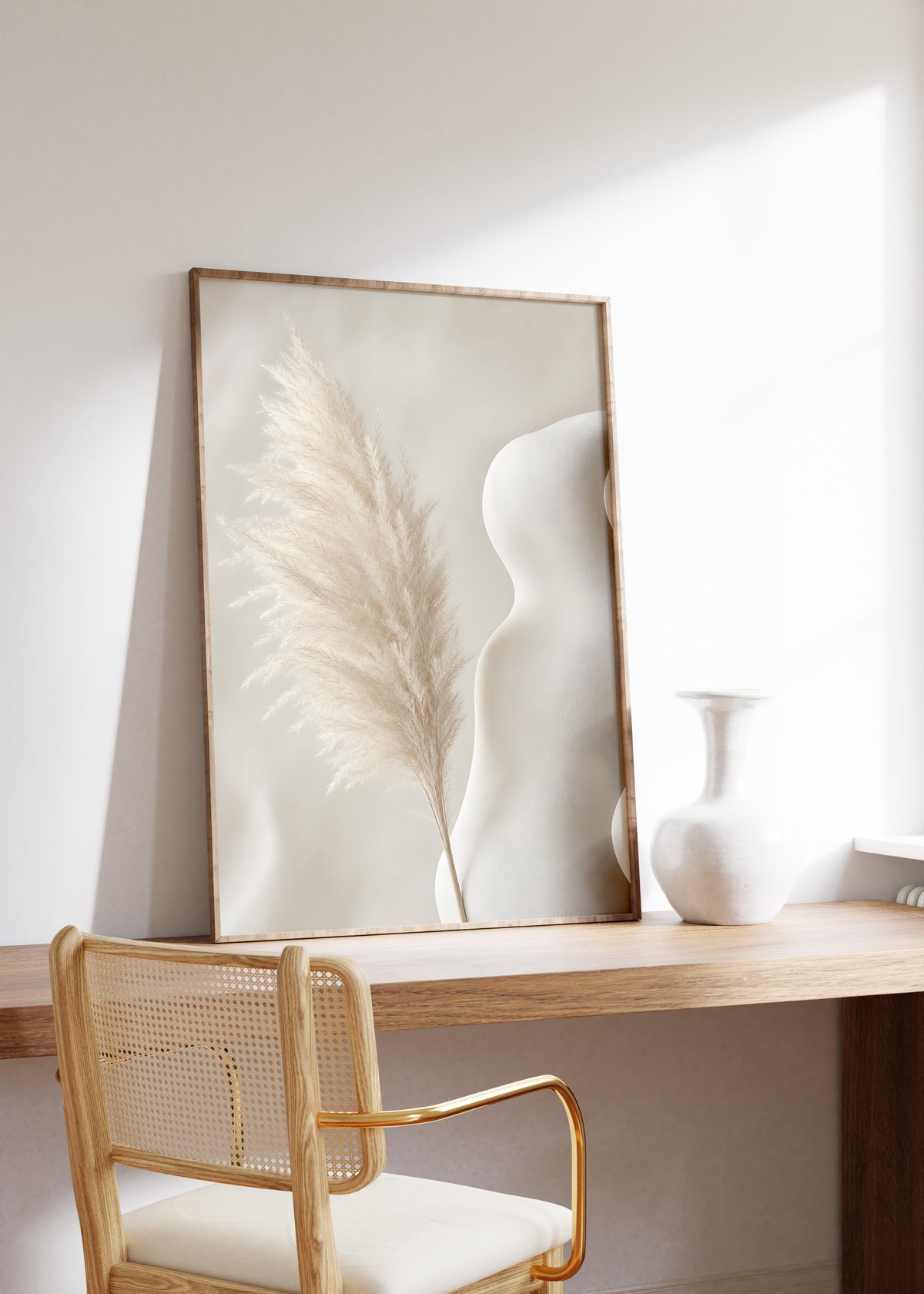 Gerahmtes Poster mit einem hellen Pampaswedel neben einer geschwungenen weißen Skulptur, auf einem Holztisch neben einer weißen Vase.