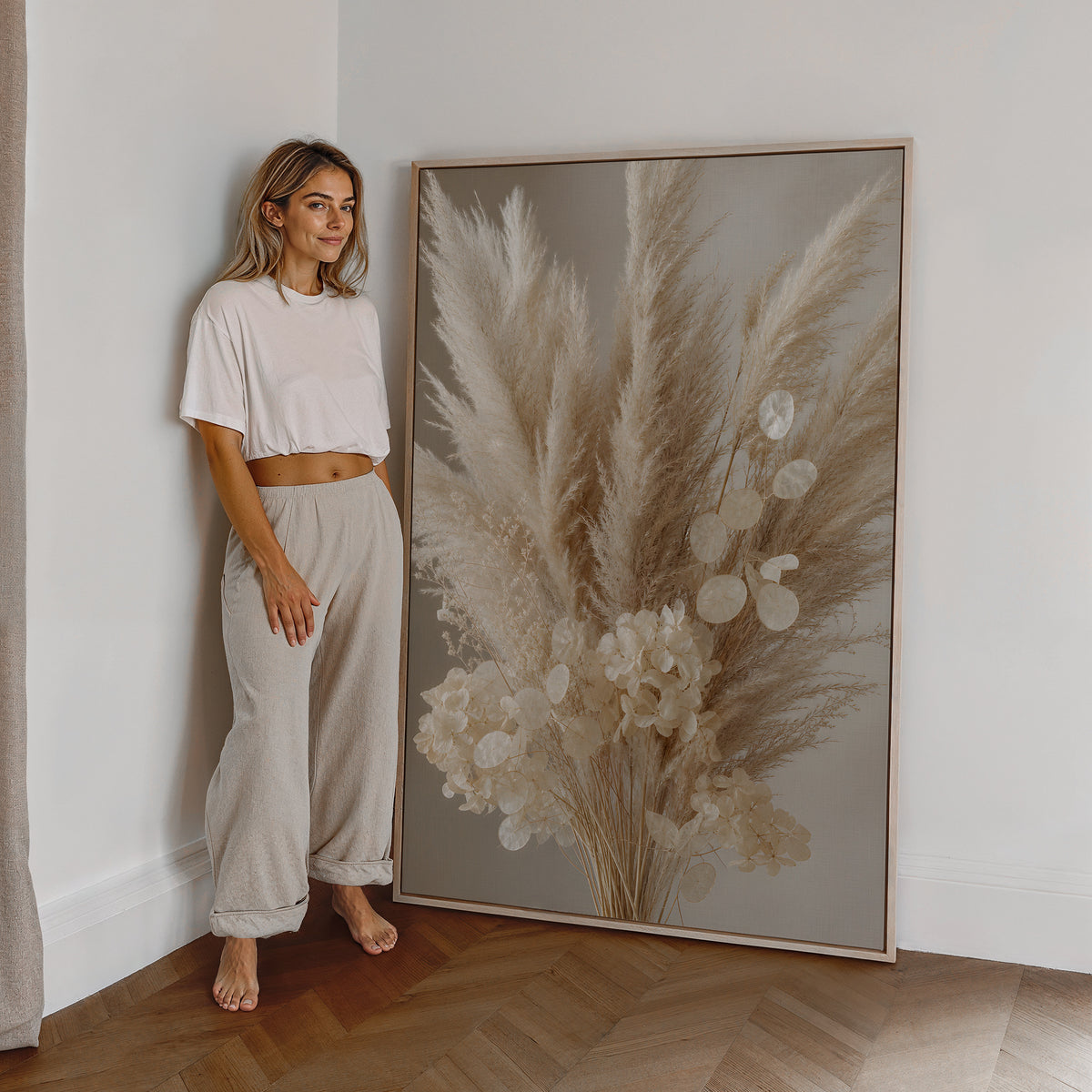 Motiv mit einem cremeweißen Bouquet aus Pampasgras, Silberblatt und hellen Blüten, als großes gerahmtes Wandbild neben einer Frau.