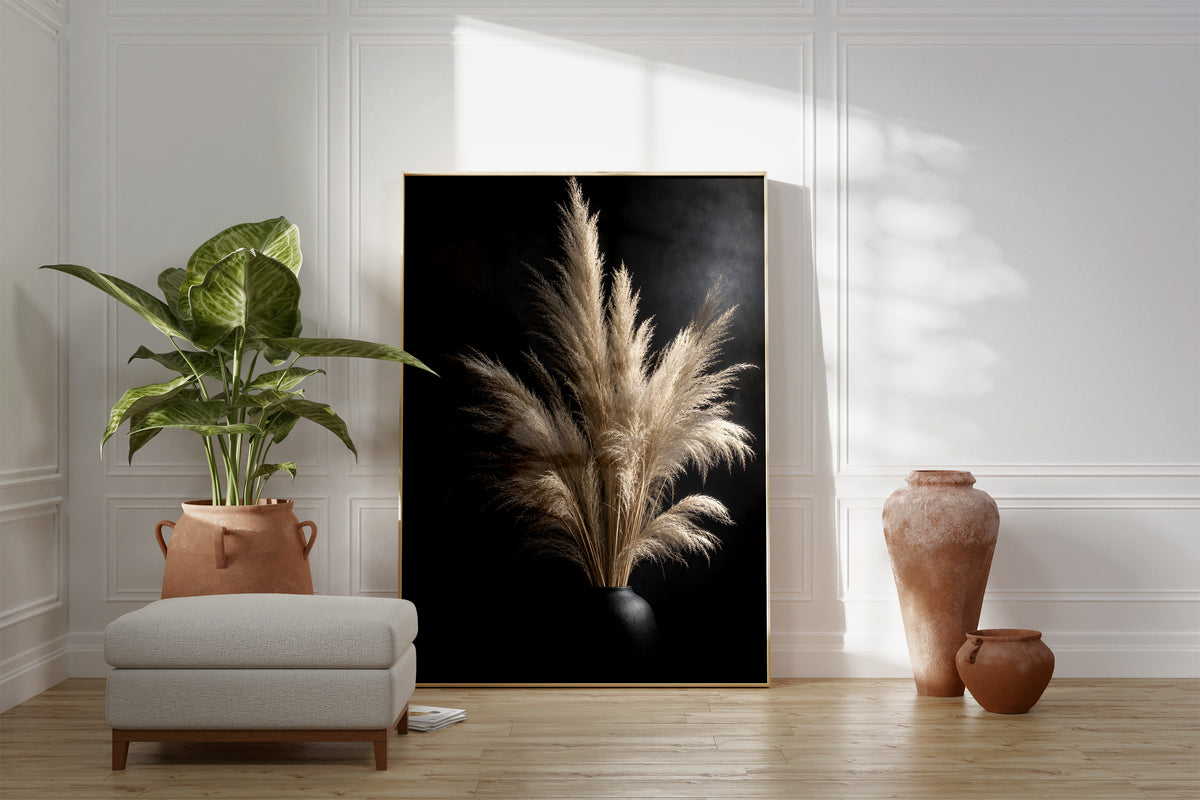 Motiv mit einem hellen Pampasbouquet in einer schwarzen Vase vor schwarzem Hintergrund, als gerahmtes Poster neben Sessel und Zimmerpflanze.