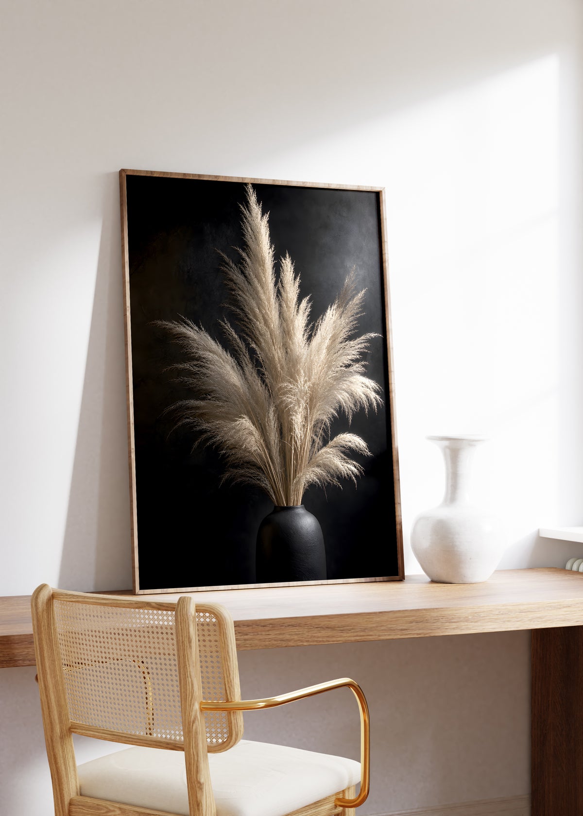 Gerahmtes Poster mit einem hellen Pampasbouquet in einer schwarzen Vase vor schwarzem Hintergrund, auf einem Holztisch neben einer weißen Vase.