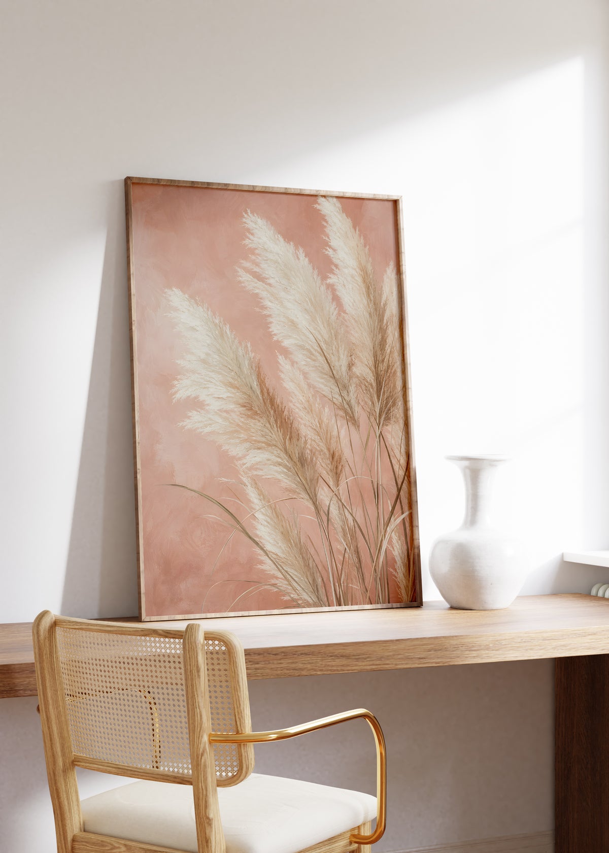 Gerahmtes Poster mit hellen Pampasgräsern vor einem strukturierten terrakottarosa Hintergrund, auf einem Holztisch neben einer weißen Vase.