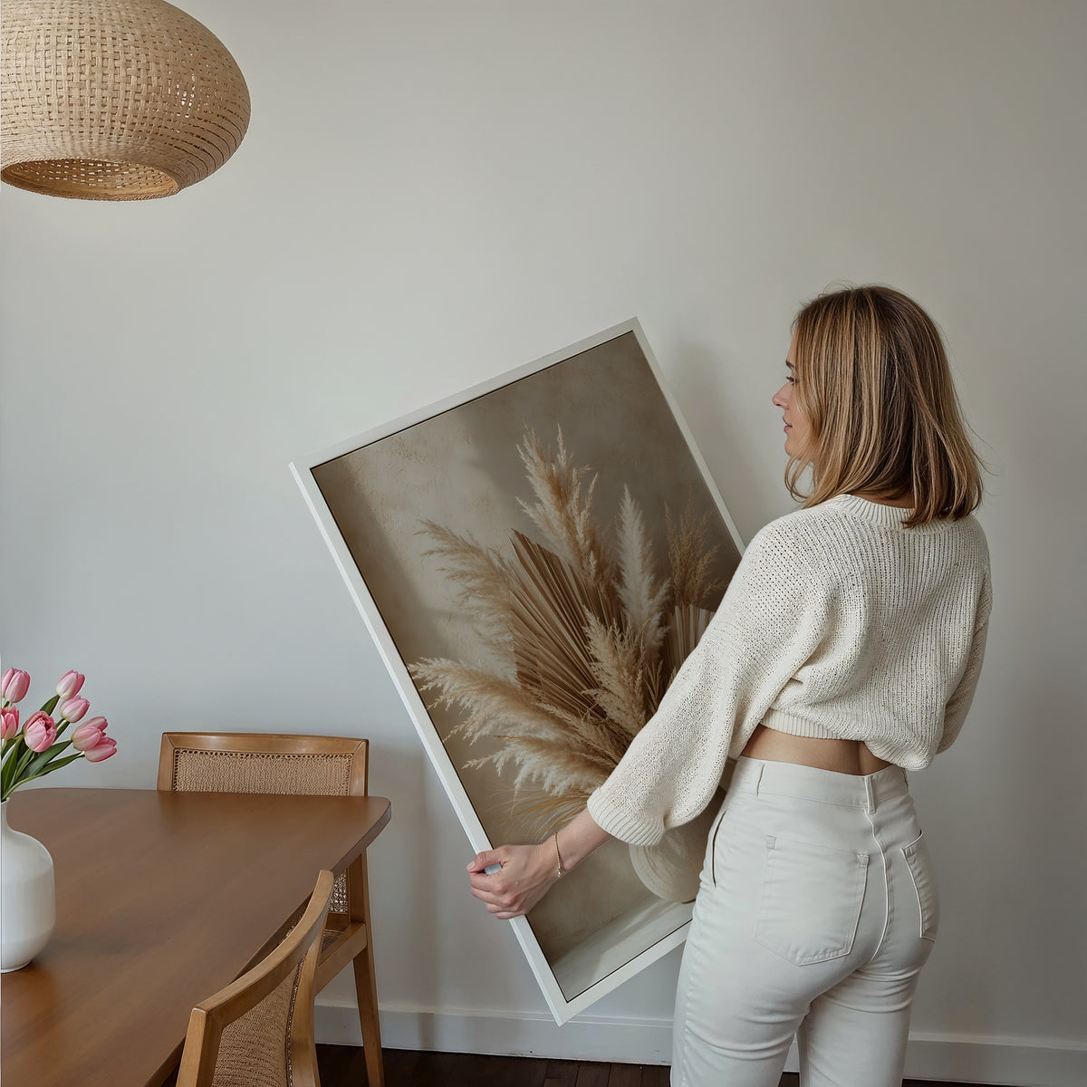 Motiv mit Pampaswedeln und getrockneten Palmfächern in einer runden beigen Vase, über einem Bett im hellen Schlafzimmer.