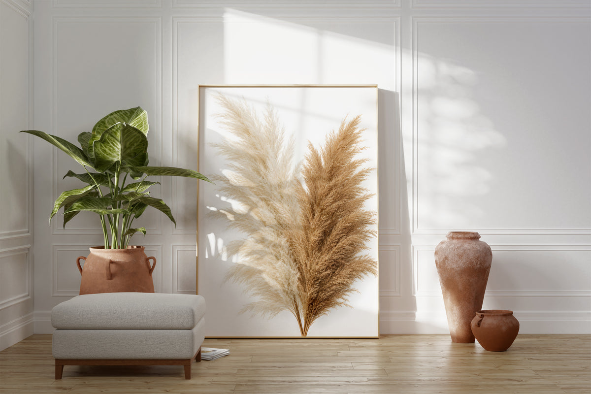 Motiv mit einem Bouquet aus cremeweißen und naturbraunen Pampaswedeln vor weißem Hintergrund, als gerahmtes Poster neben Sessel und Zimmerpflanze.