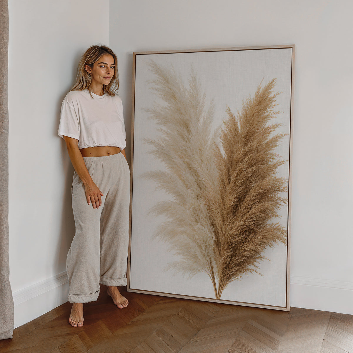 Motiv mit einem Bouquet aus cremeweißen und naturbraunen Pampaswedeln vor weißem Hintergrund, als großes gerahmtes Wandbild neben einer Frau.