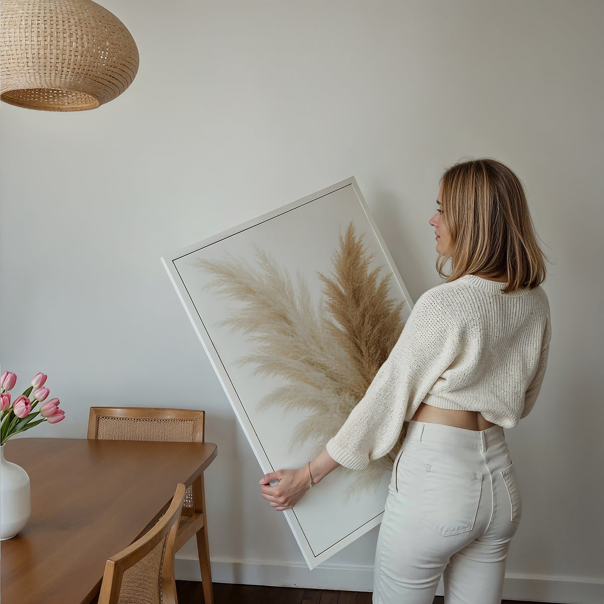 Motiv mit einem Bouquet aus cremeweißen und naturbraunen Pampaswedeln vor weißem Hintergrund, über einem Bett im hellen Schlafzimmer.