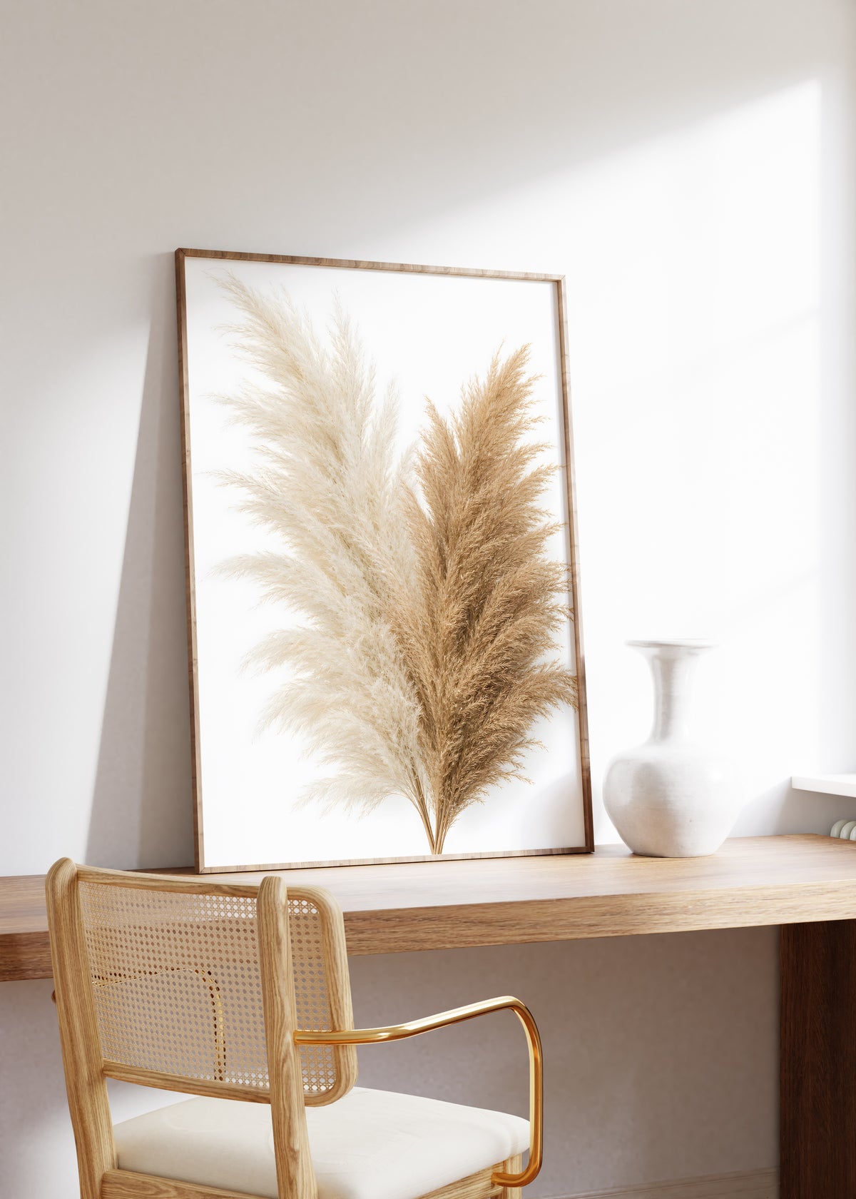 Gerahmtes Poster mit einem Bouquet aus cremeweißen und naturbraunen Pampaswedeln vor weißem Hintergrund, auf einem Holztisch neben einer weißen Vase.