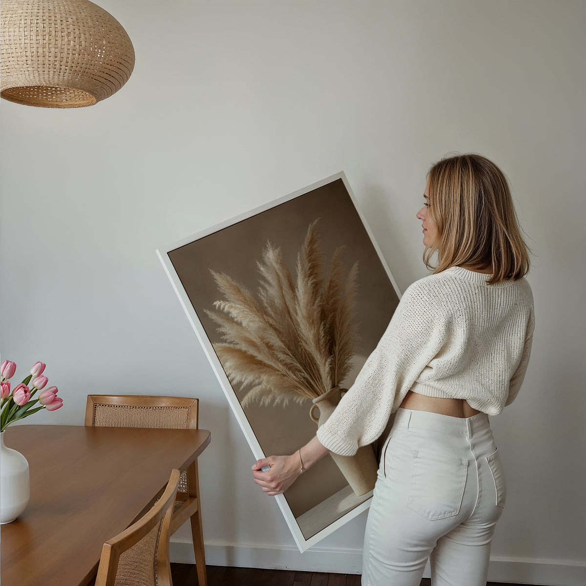 Motiv mit einem Pampasbouquet in einer beigefarbenen Henkelvase neben hellem Stoff, über einem Bett im hellen Schlafzimmer.