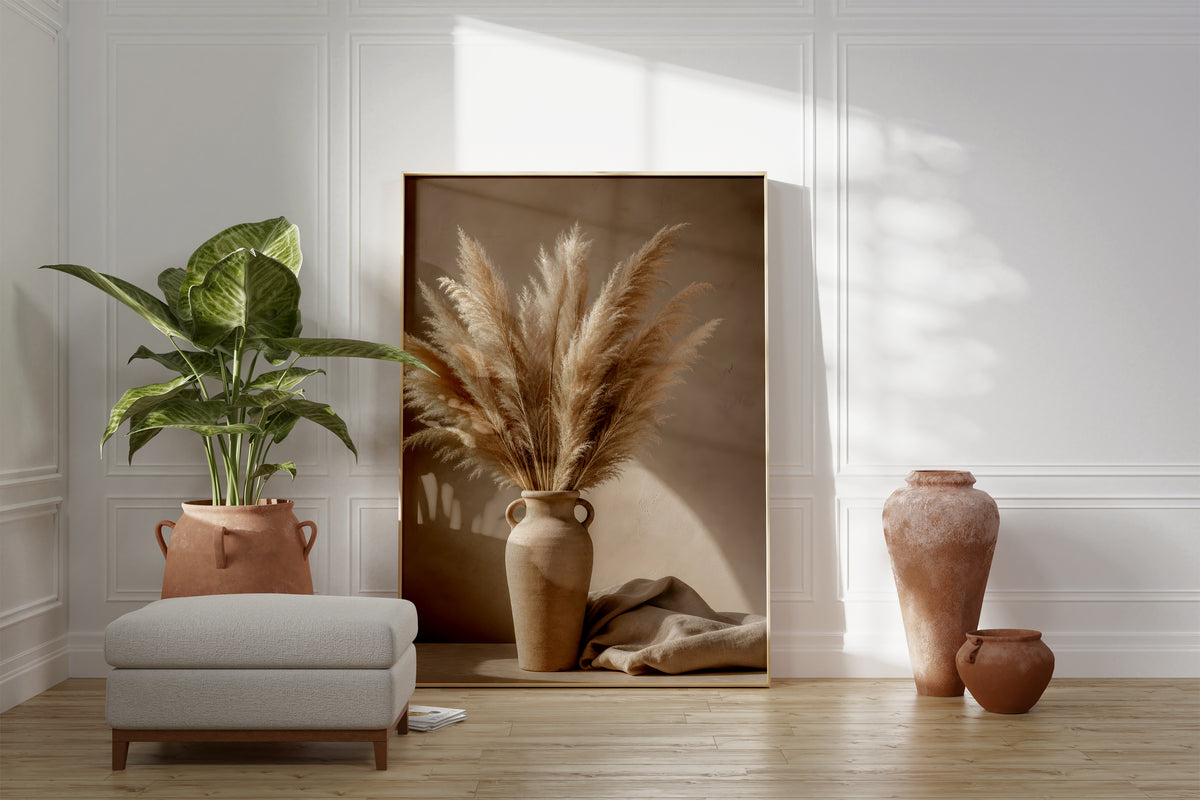 Motiv mit einem Pampasbouquet in einer beigefarbenen Henkelvase neben hellem Stoff, als gerahmtes Poster neben Sessel und Zimmerpflanze.