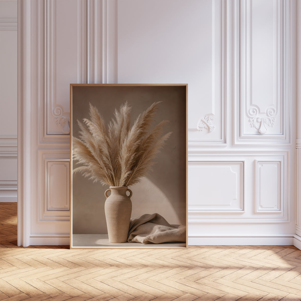 Gerahmtes Poster mit einem Pampasbouquet in einer beigefarbenen Henkelvase neben hellem Stoff, vor einer weißen Wand mit Zierleisten.