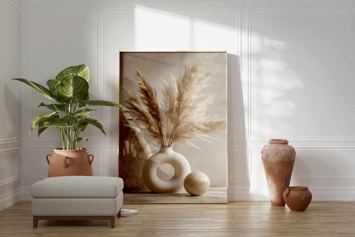Motiv mit einem cremebraunen Pampasbouquet in einer weißen Ringvase neben einer Steinkugel, als gerahmtes Poster neben Sessel und Zimmerpflanze.