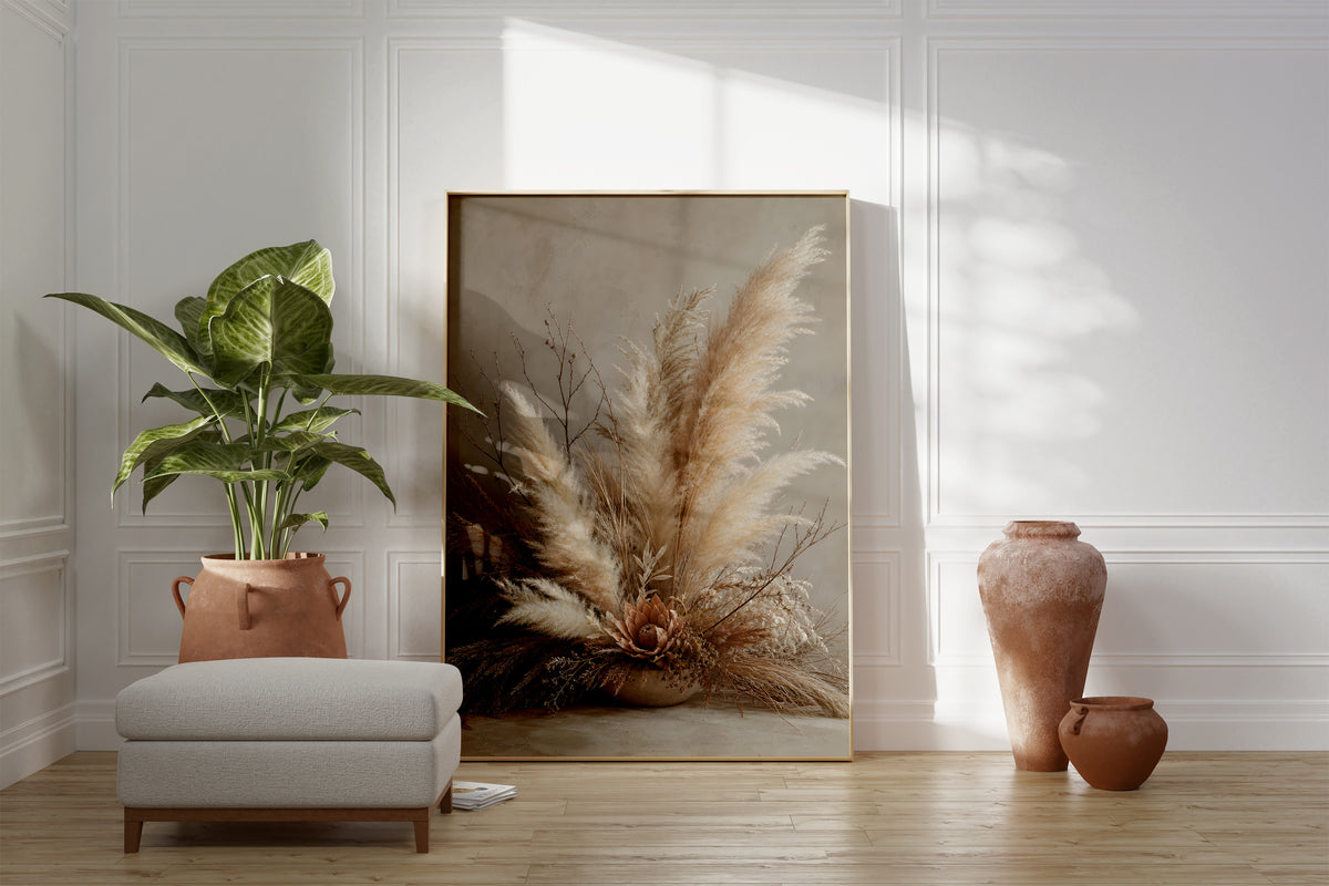 Motiv mit einem niedrigen Pampasgesteck mit feinen Zweigen und einer braunen Blüte in einer Schale, als gerahmtes Poster neben Sessel und Zimmerpflanze.