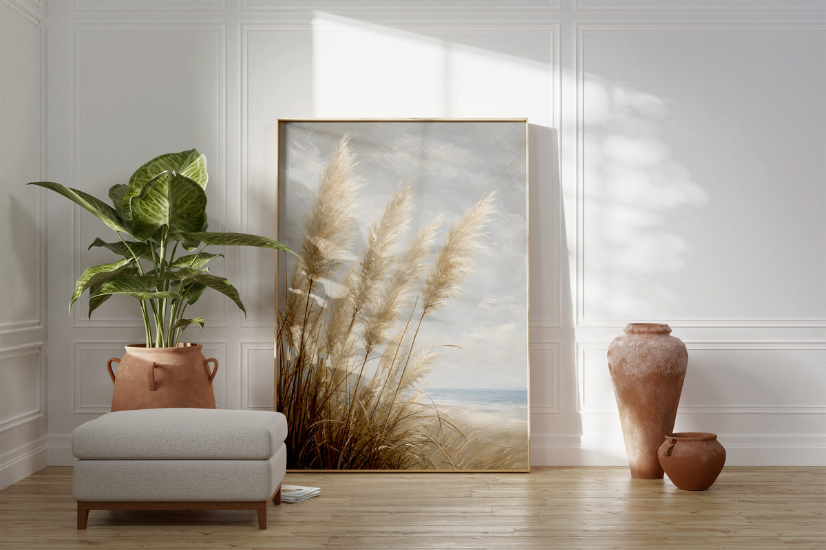 Motiv mit hellen Pampasgräsern am Meer unter einem wolkigen Himmel in malerischer Optik, als gerahmtes Poster neben Sessel und Zimmerpflanze.
