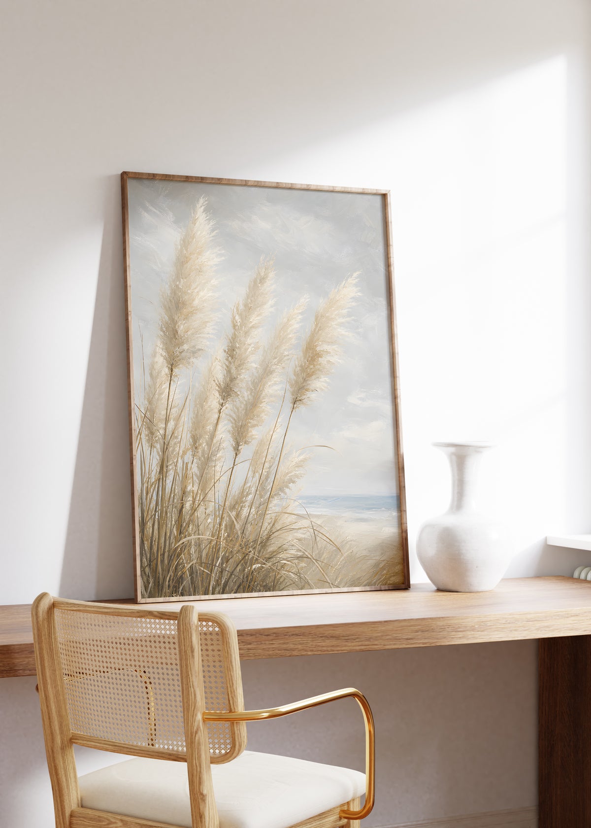 Gerahmtes Poster mit hellen Pampasgräsern am Meer unter einem wolkigen Himmel in malerischer Optik, auf einem Holztisch neben einer weißen Vase.
