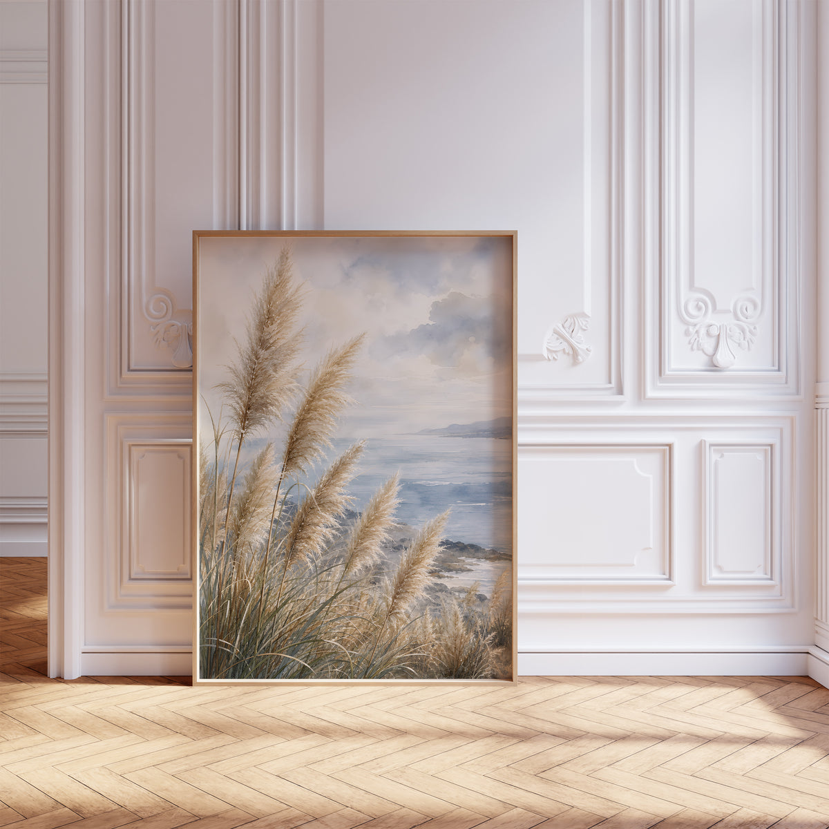 Gerahmtes Poster mit Pampasgräsern an einer blauen Küste unter Wolken in Aquarelloptik, vor einer weißen Wand mit Zierleisten.
