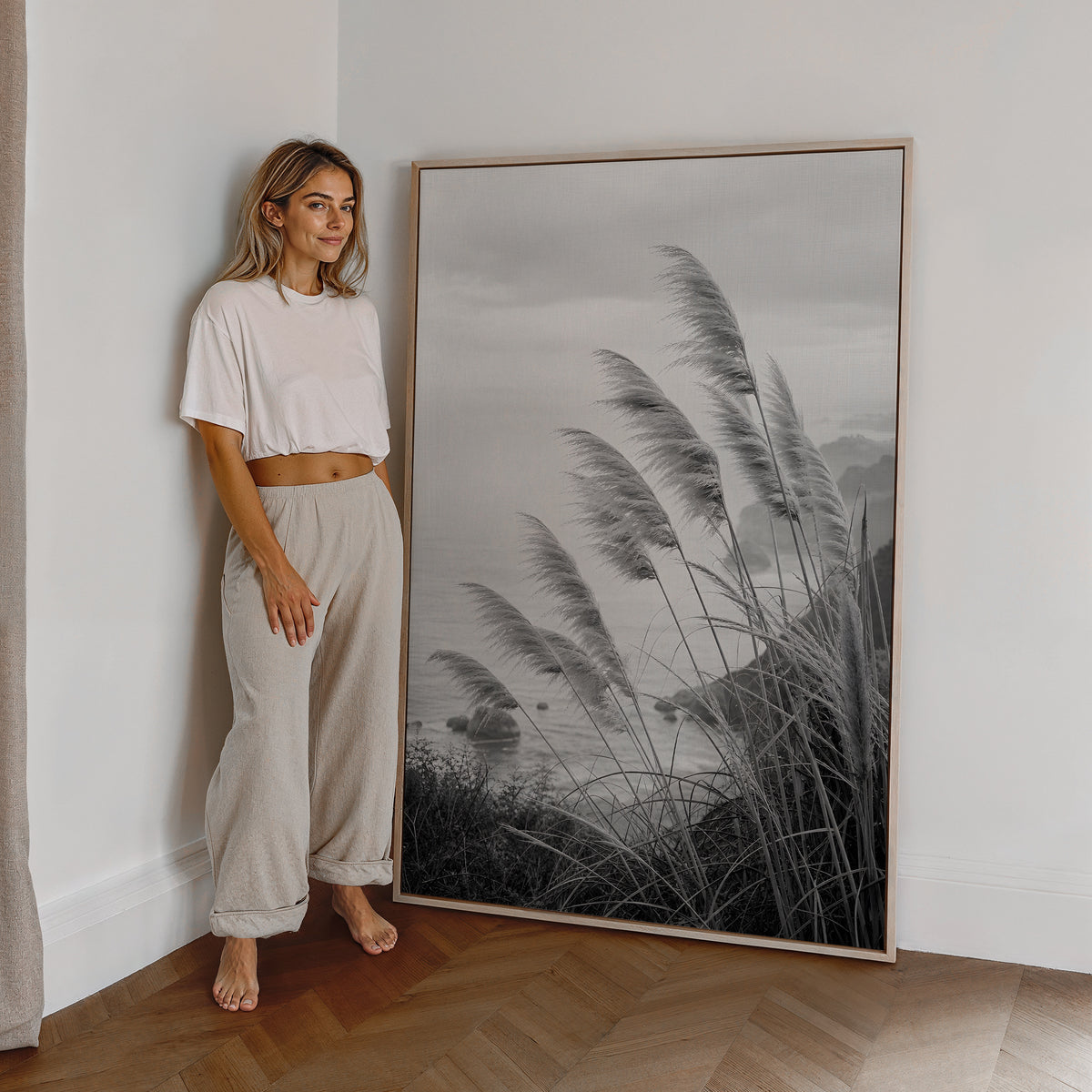 Motiv mit Pampasgräsern an einer Küste in Schwarz-Weiß, als großes gerahmtes Wandbild neben einer Frau.
