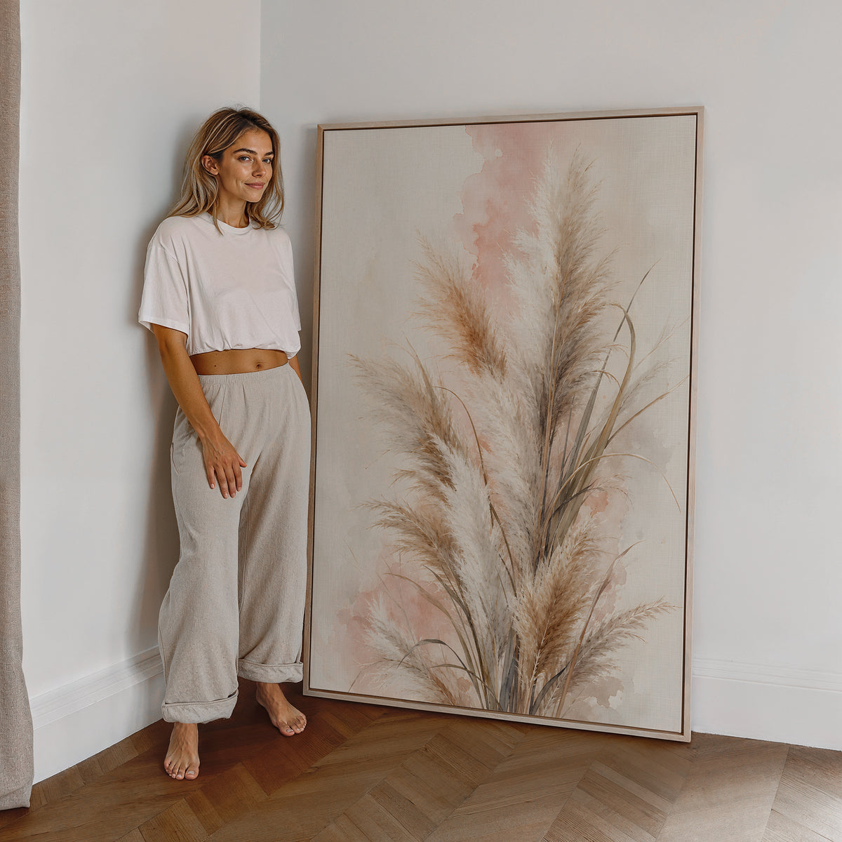 Motiv mit beigebraunen Pampasgräsern vor rosigen Aquarellflächen, als großes gerahmtes Wandbild neben einer Frau.
