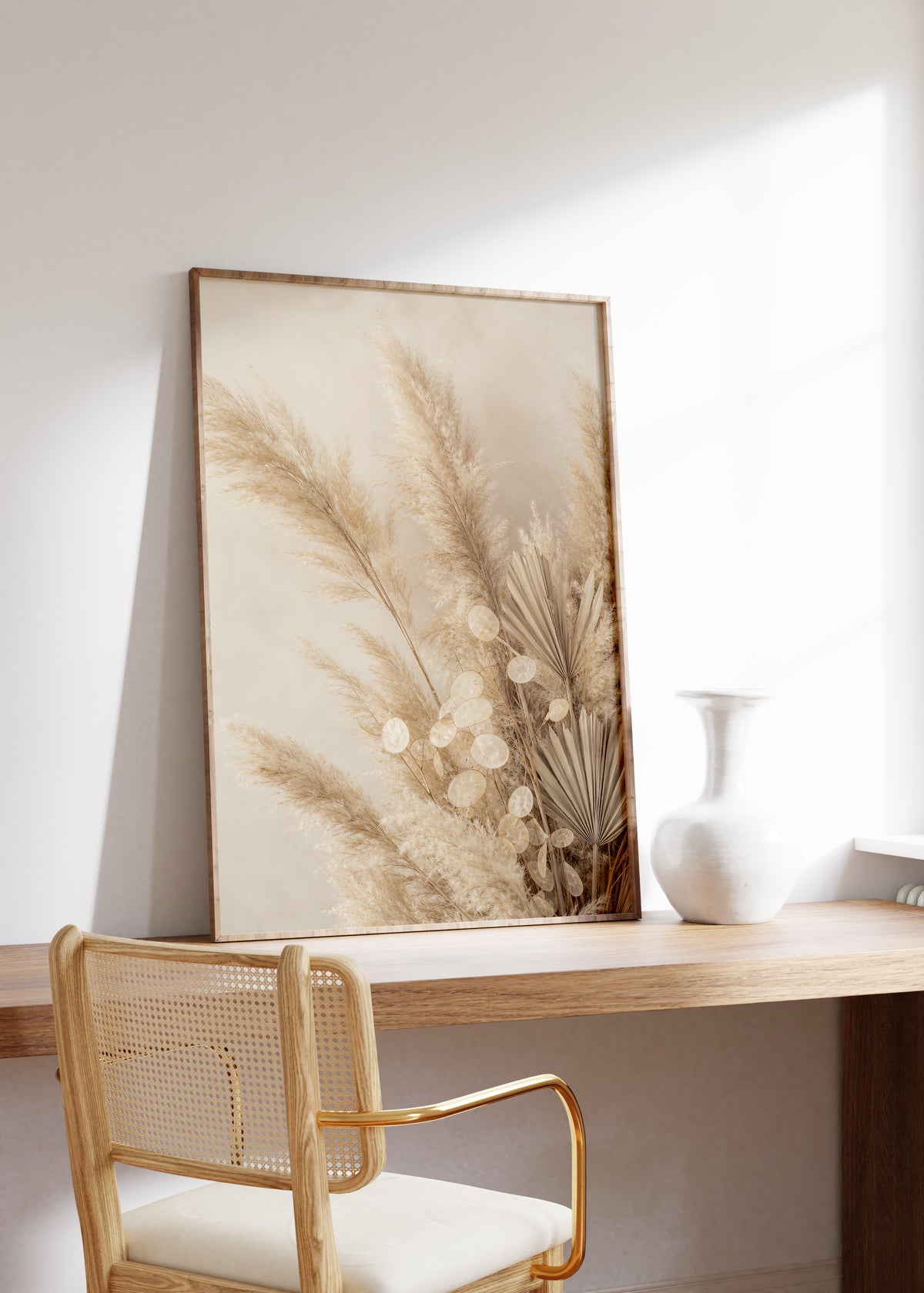 Gerahmtes Poster mit einem beigefarbenen Arrangement aus Pampasgras, Silberblatt und getrocknetem Palmfächer, auf einem Holztisch neben einer weißen Vase.