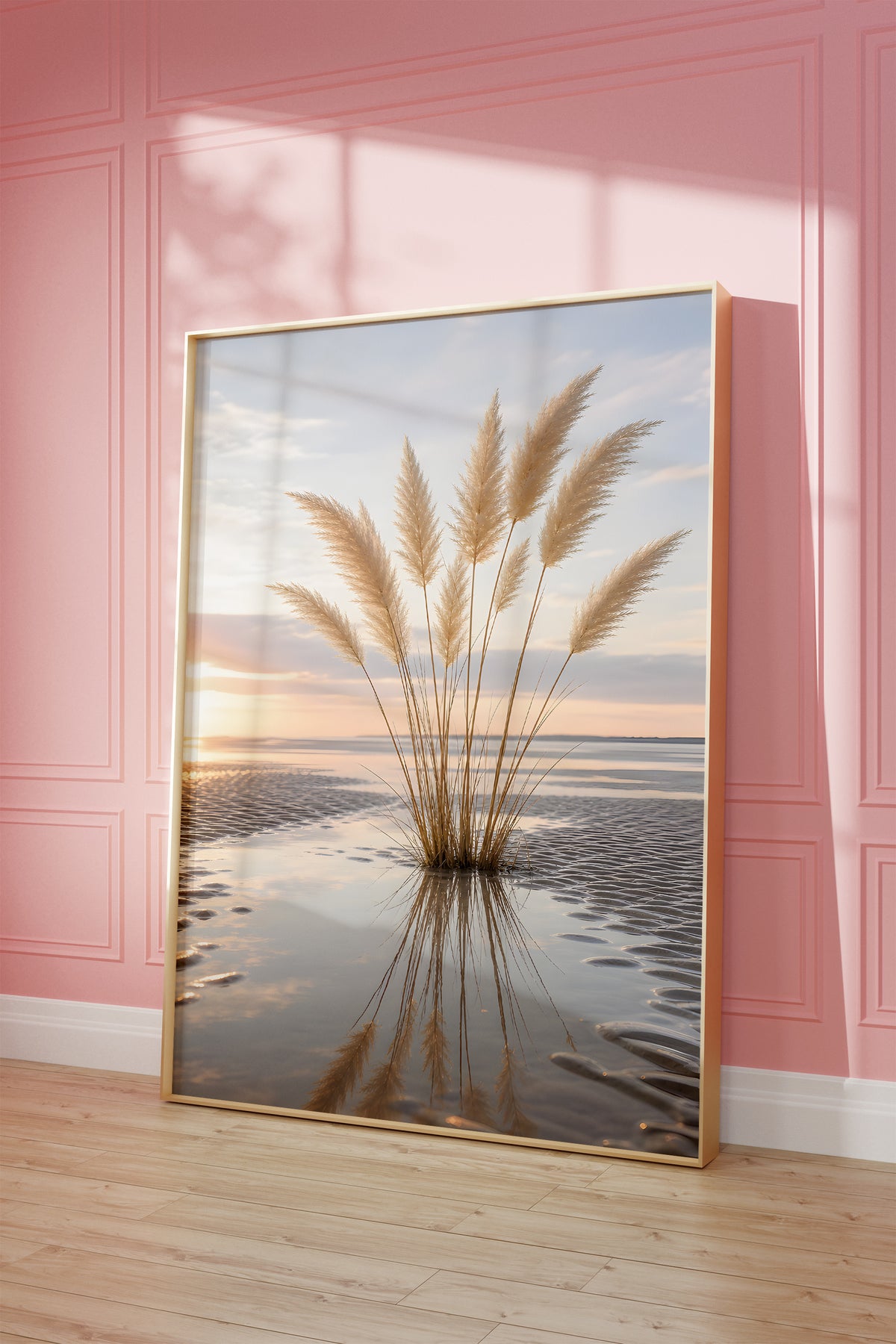 Motiv mit einem Pampasgrasbüschel mit Spiegelung im nassen Strandsand bei Sonnenuntergang, als gerahmtes Poster vor einer rosafarbenen Wand.