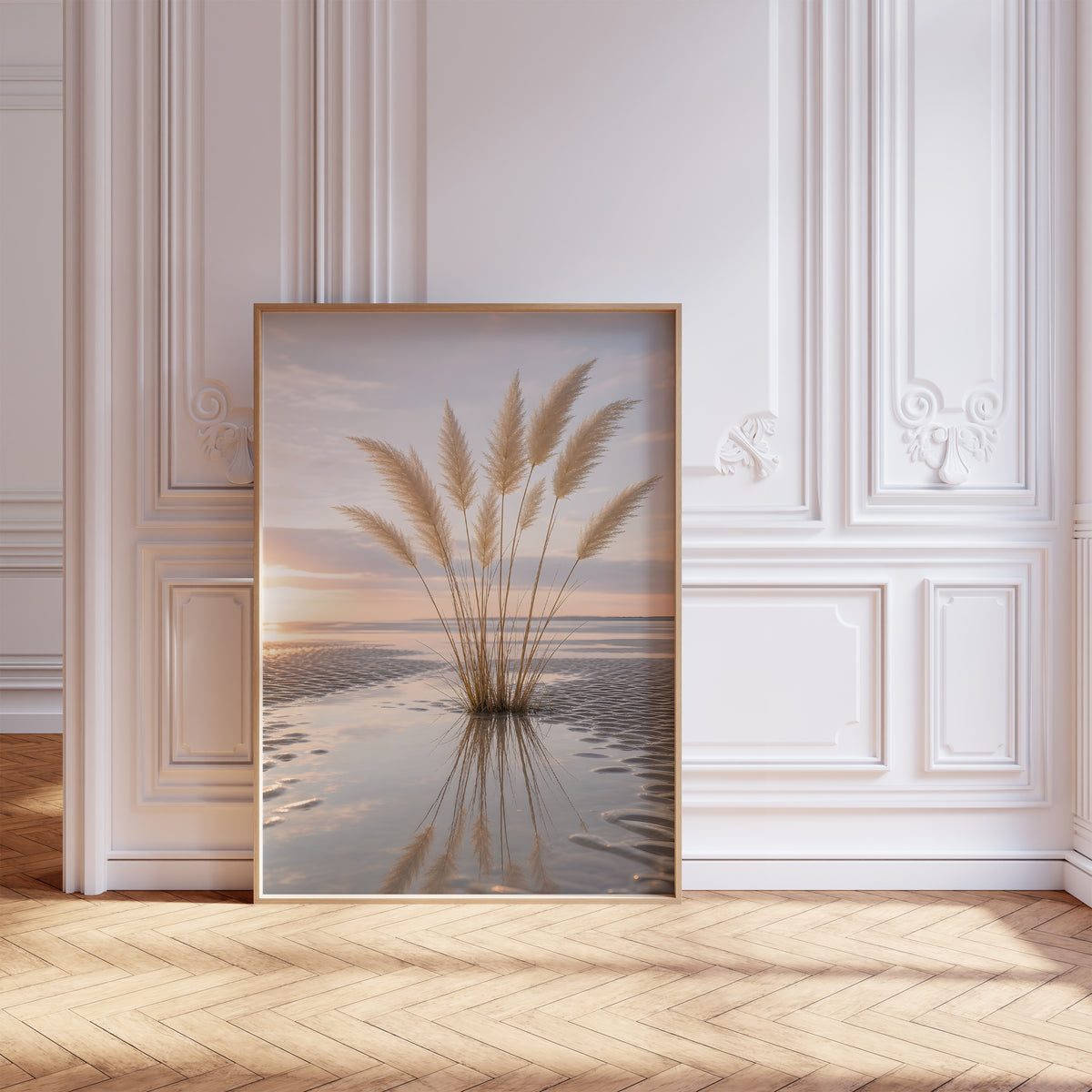 Gerahmtes Poster mit einem Pampasgrasbüschel mit Spiegelung im nassen Strandsand bei Sonnenuntergang, vor einer weißen Wand mit Zierleisten.