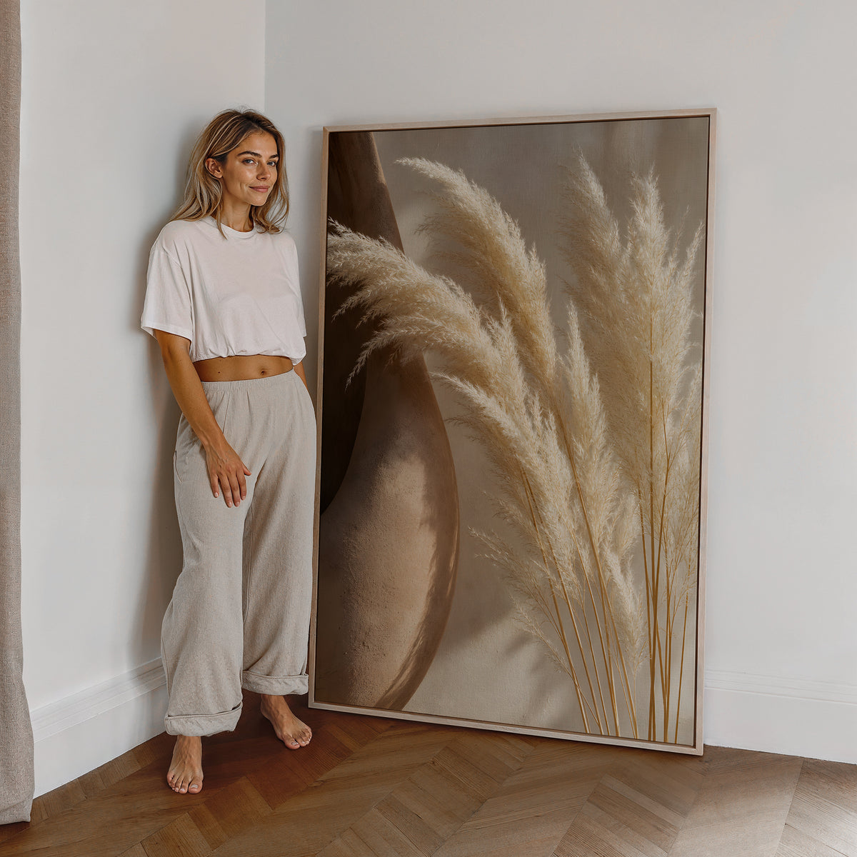 Motiv mit hellen Pampaswedeln neben einer großen braunen Tonvase, als großes gerahmtes Wandbild neben einer Frau.