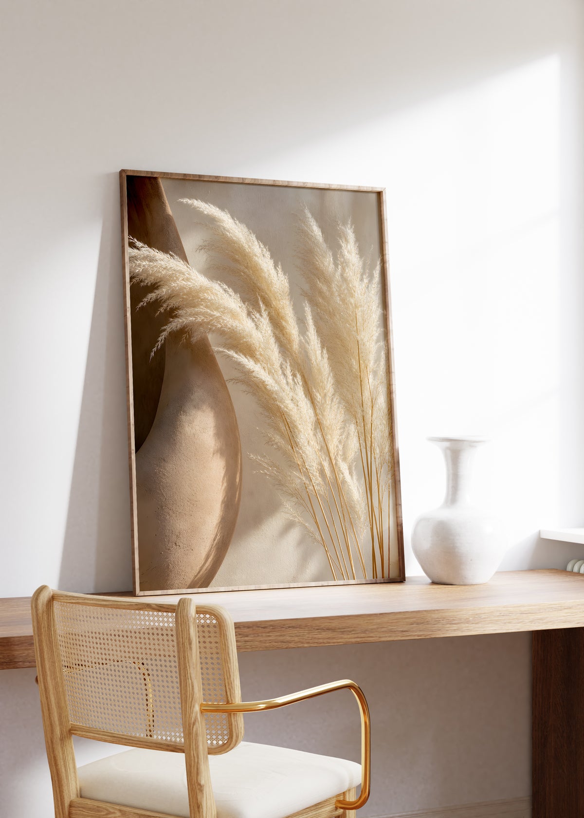 Gerahmtes Poster mit hellen Pampaswedeln neben einer großen braunen Tonvase, auf einem Holztisch neben einer weißen Vase.