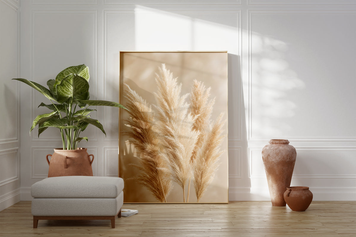 Motiv mit mehreren flauschigen Pampaswedeln in Creme und Beige vor weich verschwommenem Hintergrund, als gerahmtes Poster neben Sessel und Zimmerpflanze.