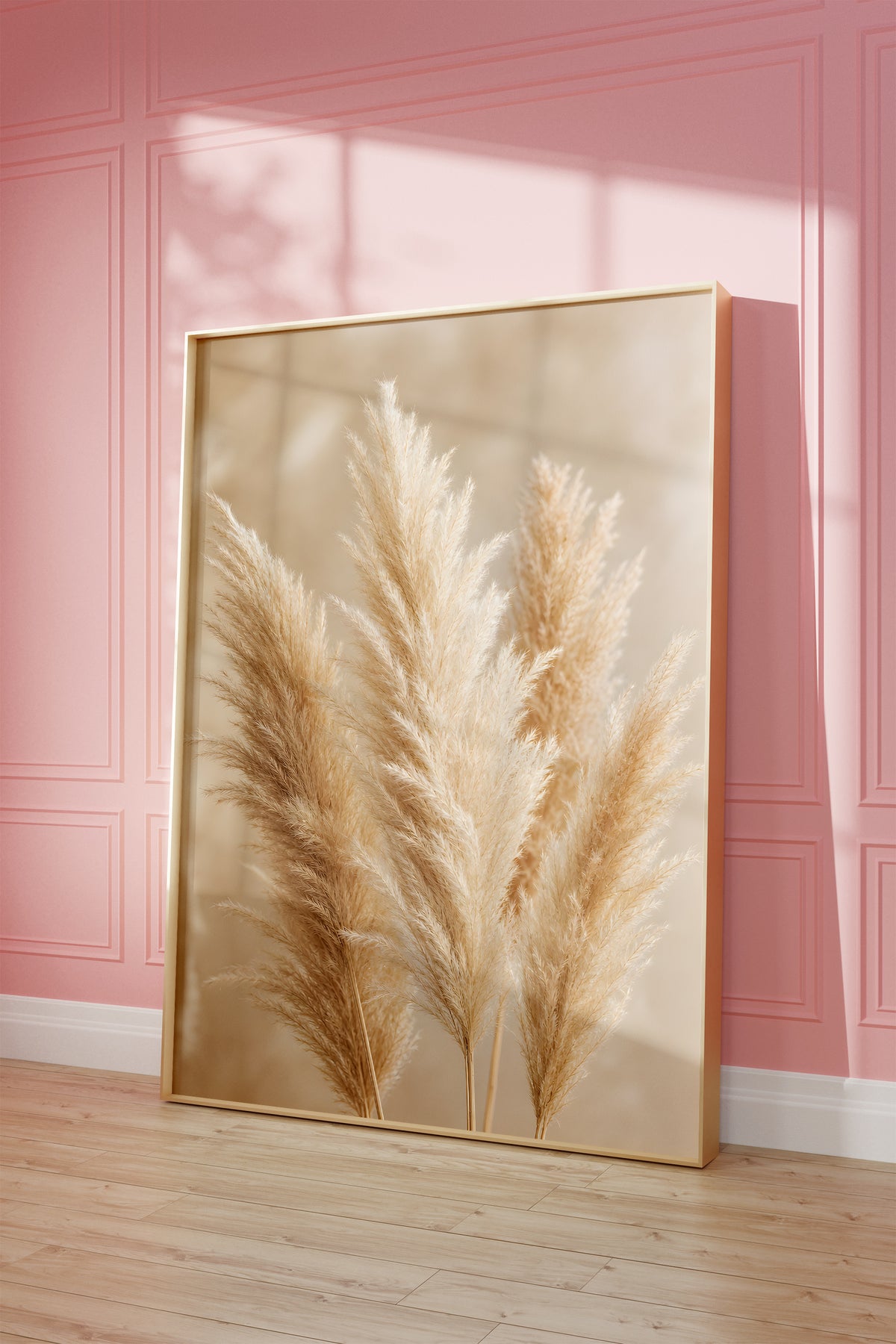 Motiv mit mehreren flauschigen Pampaswedeln in Creme und Beige vor weich verschwommenem Hintergrund, als gerahmtes Poster vor einer rosafarbenen Wand.