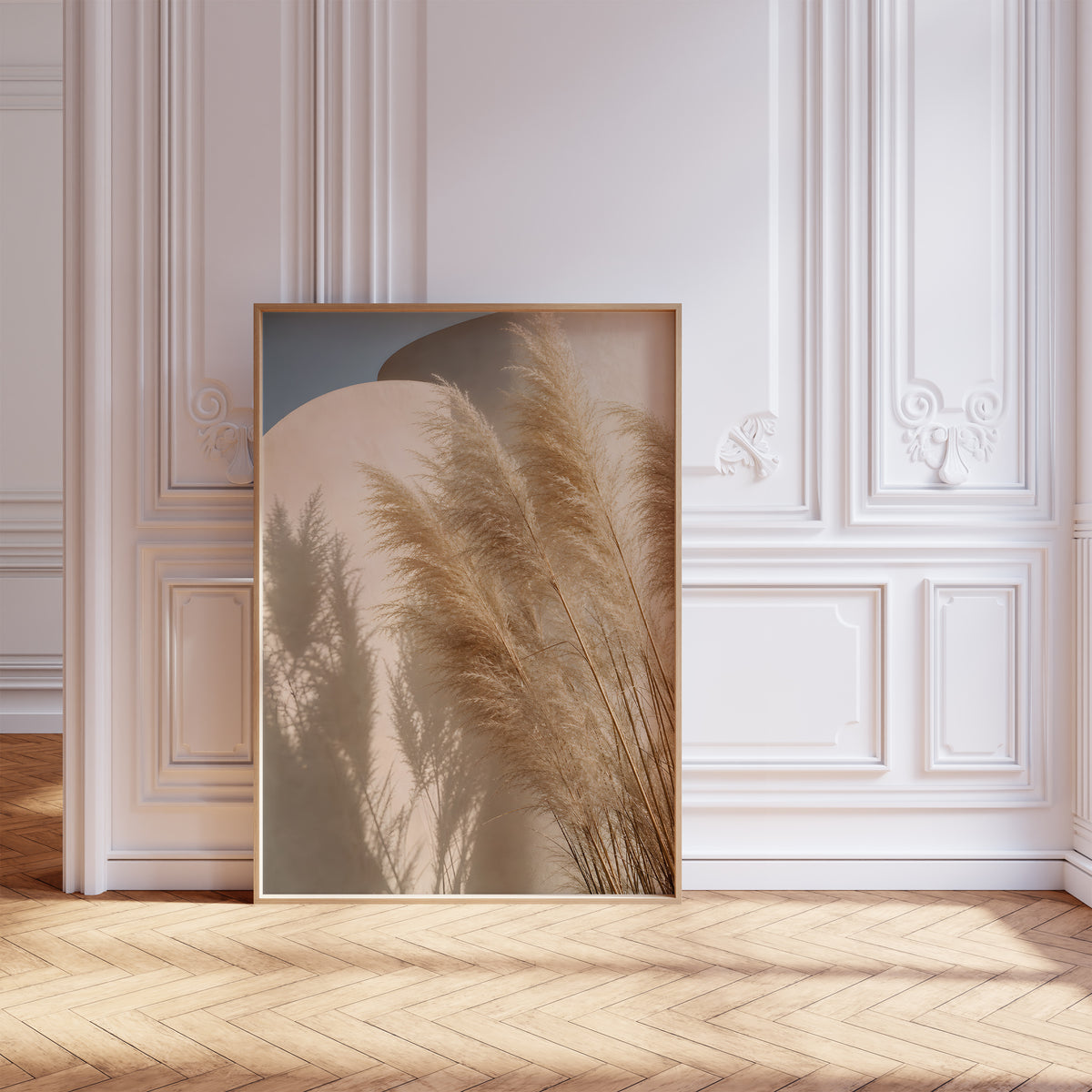 Gerahmtes Poster mit Pampasgräsern und ihren Schatten vor geschwungenen sandfarbenen Wänden unter blauem Himmel, vor einer weißen Wand mit Zierleisten.