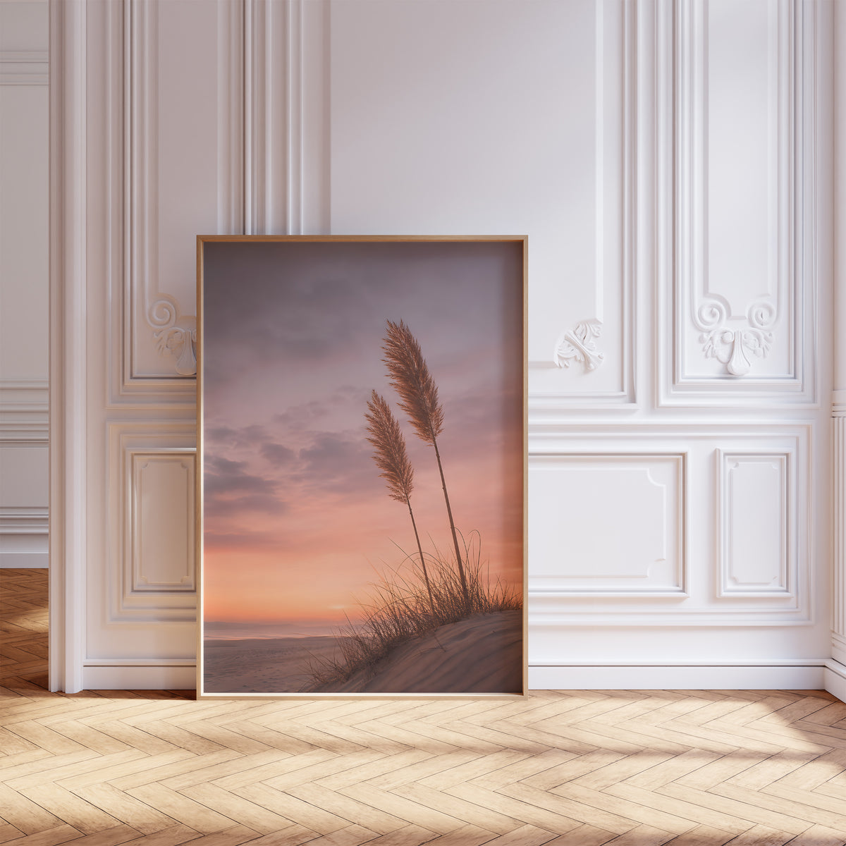 Gerahmtes Poster mit zwei Pampaswedeln auf einer Düne vor einem rosa-orangefarbenen Abendhimmel, vor einer weißen Wand mit Zierleisten.