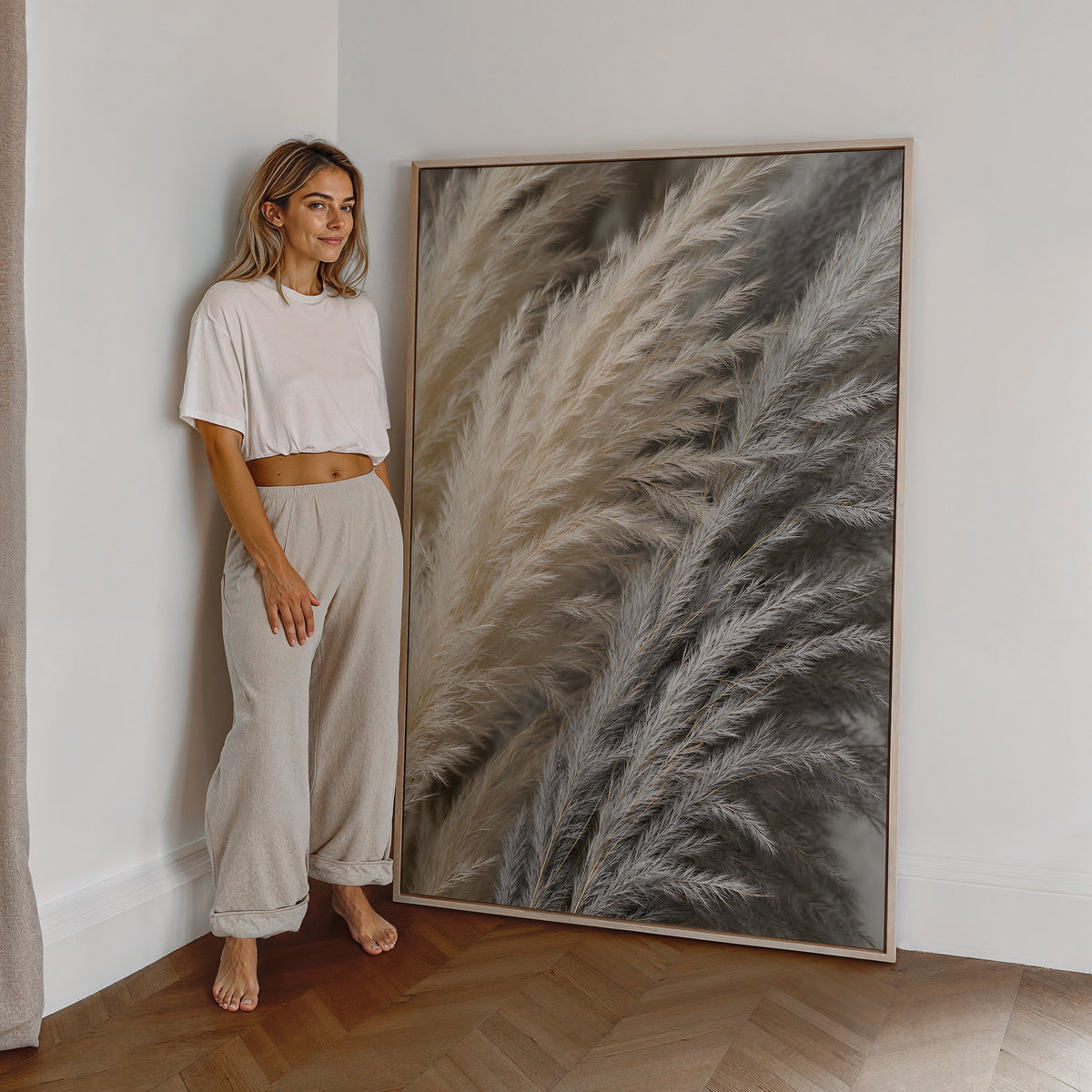 Motiv mit einer dichten Nahaufnahme von Pampasfasern in Beige und Silbergrau, als großes gerahmtes Wandbild neben einer Frau.