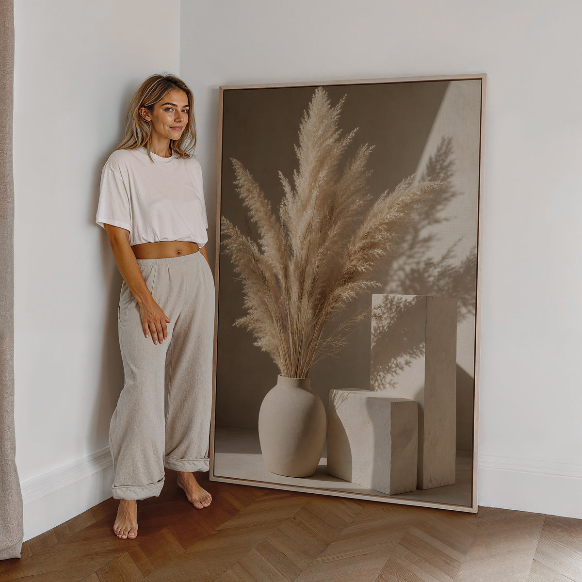 Motiv mit einer hellen Vase mit Pampasgras neben geometrischen Steinformen und Schatten, als großes gerahmtes Wandbild neben einer Frau.