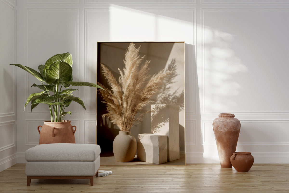 Motiv mit einer hellen Vase mit Pampasgras neben geometrischen Steinformen und Schatten, als gerahmtes Poster neben Sessel und Zimmerpflanze.