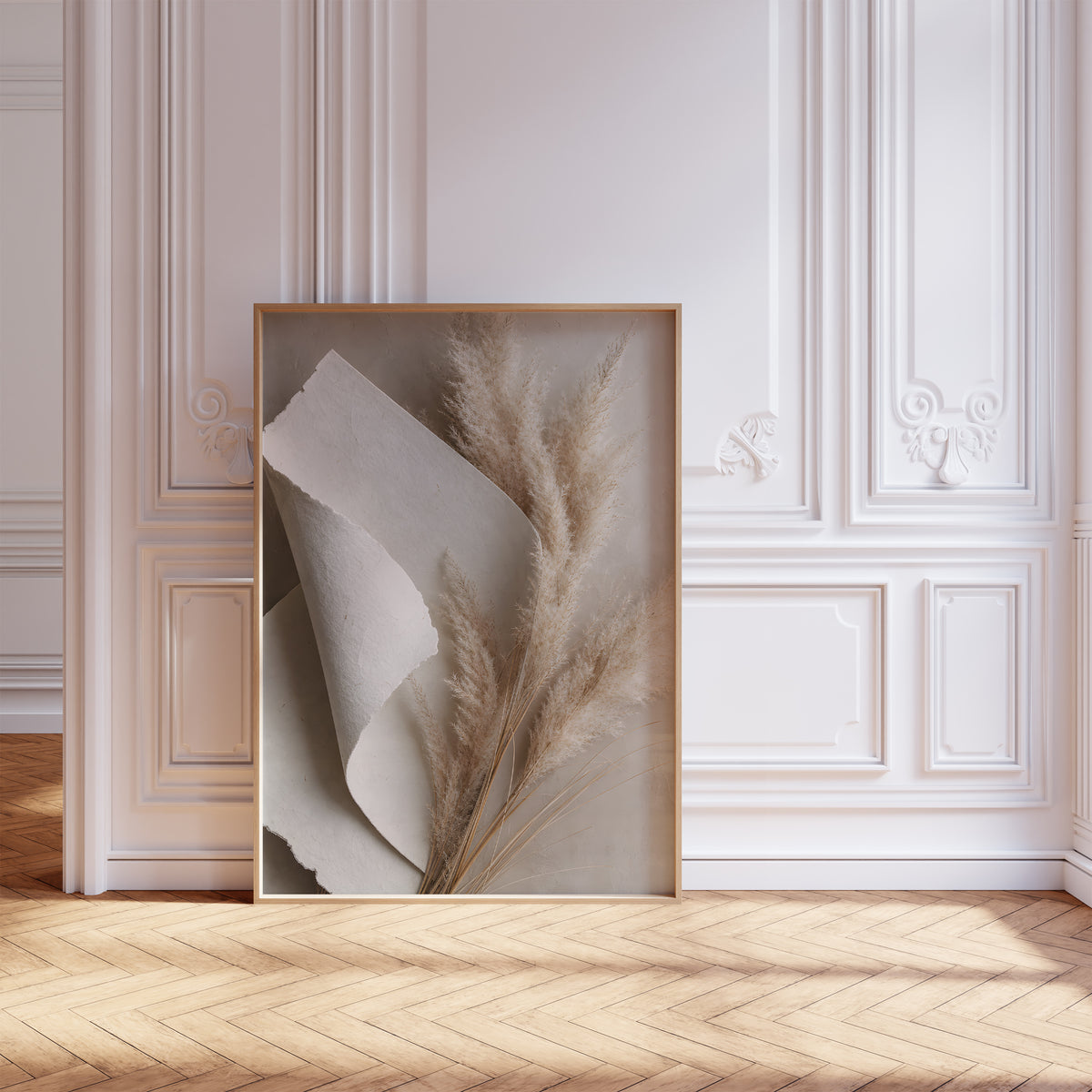 Gerahmtes Poster mit beigen Pampaswedeln neben gefaltetem weißem Naturpapier, vor einer weißen Wand mit Zierleisten.