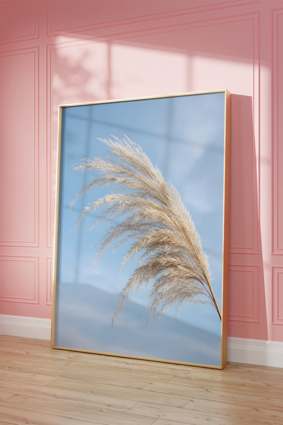 Motiv mit einem gebogenen hellen Pampaswedel vor blauem Himmel, als gerahmtes Poster vor einer rosafarbenen Wand.