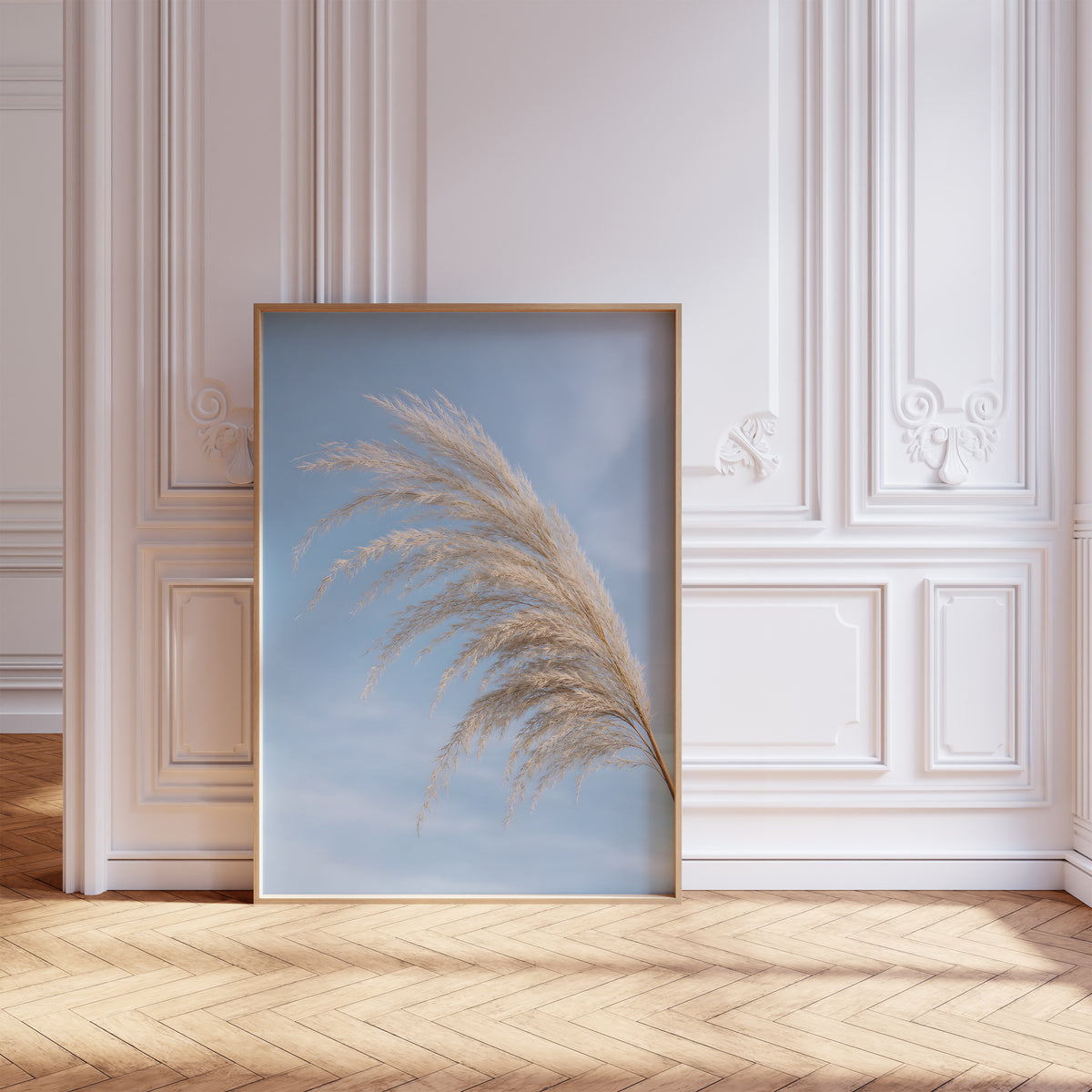 Gerahmtes Poster mit einem gebogenen hellen Pampaswedel vor blauem Himmel, vor einer weißen Wand mit Zierleisten.