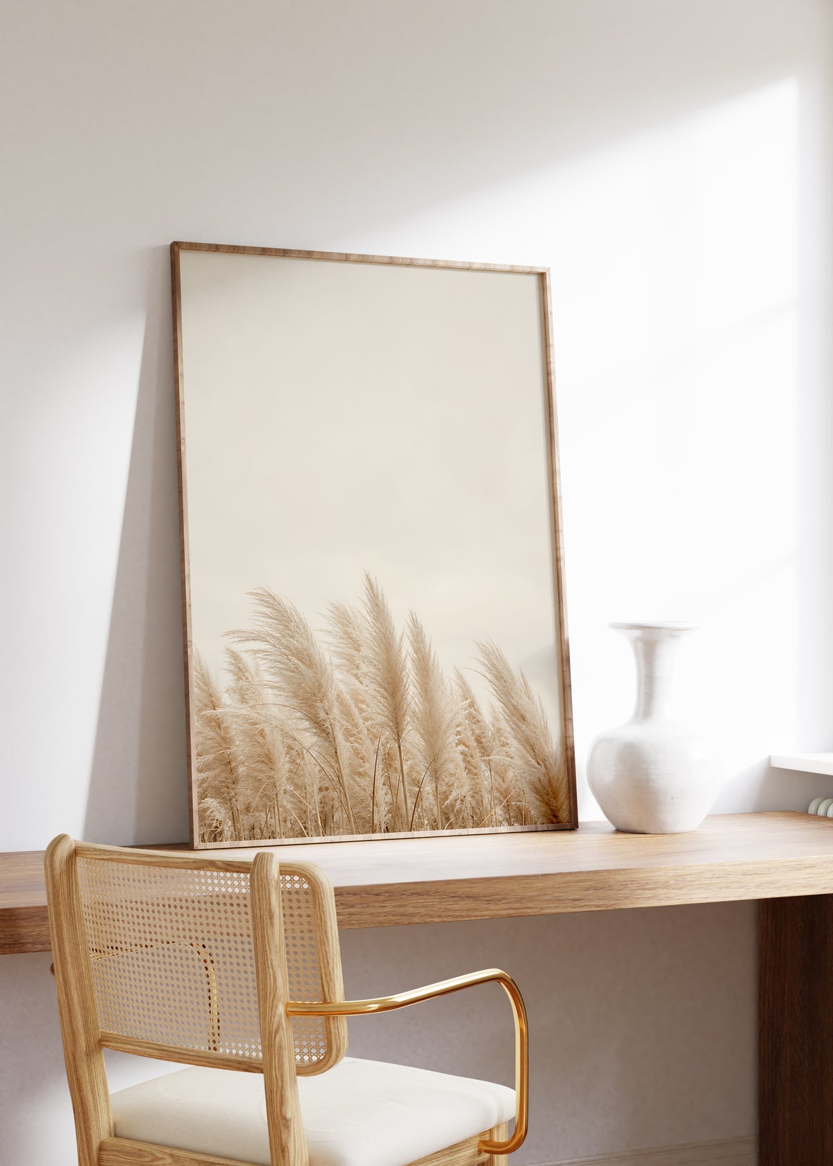 Gerahmtes Poster mit einer niedrigen Reihe beiger Pampasgräser unter einer großen hellbeigen Fläche, auf einem Holztisch neben einer weißen Vase.