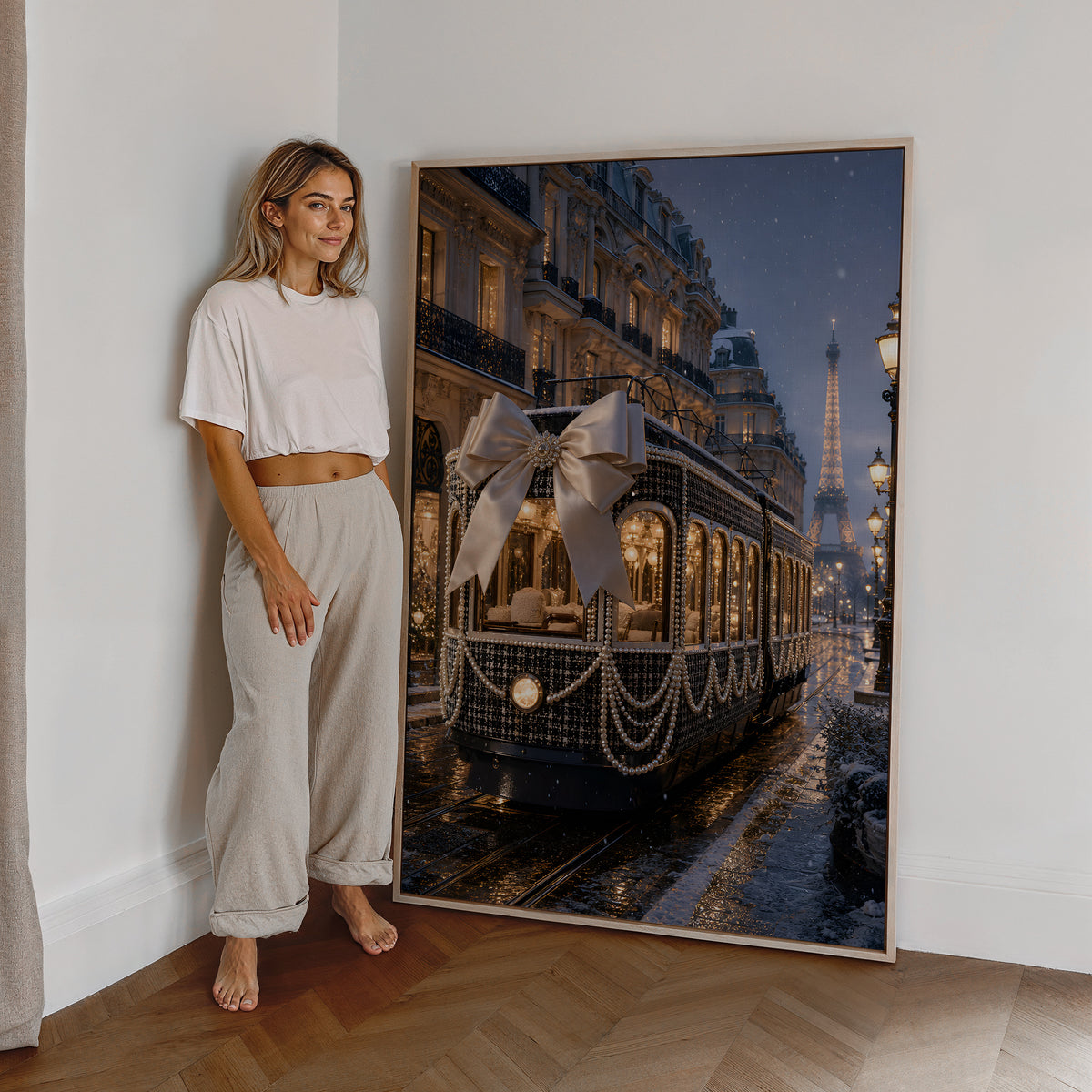 Motiv mit dunkler Pariser Straßenbahn mit großer Satinschleife und Perlenketten im Abendlicht, als großes gerahmtes Wandbild neben einer Frau.