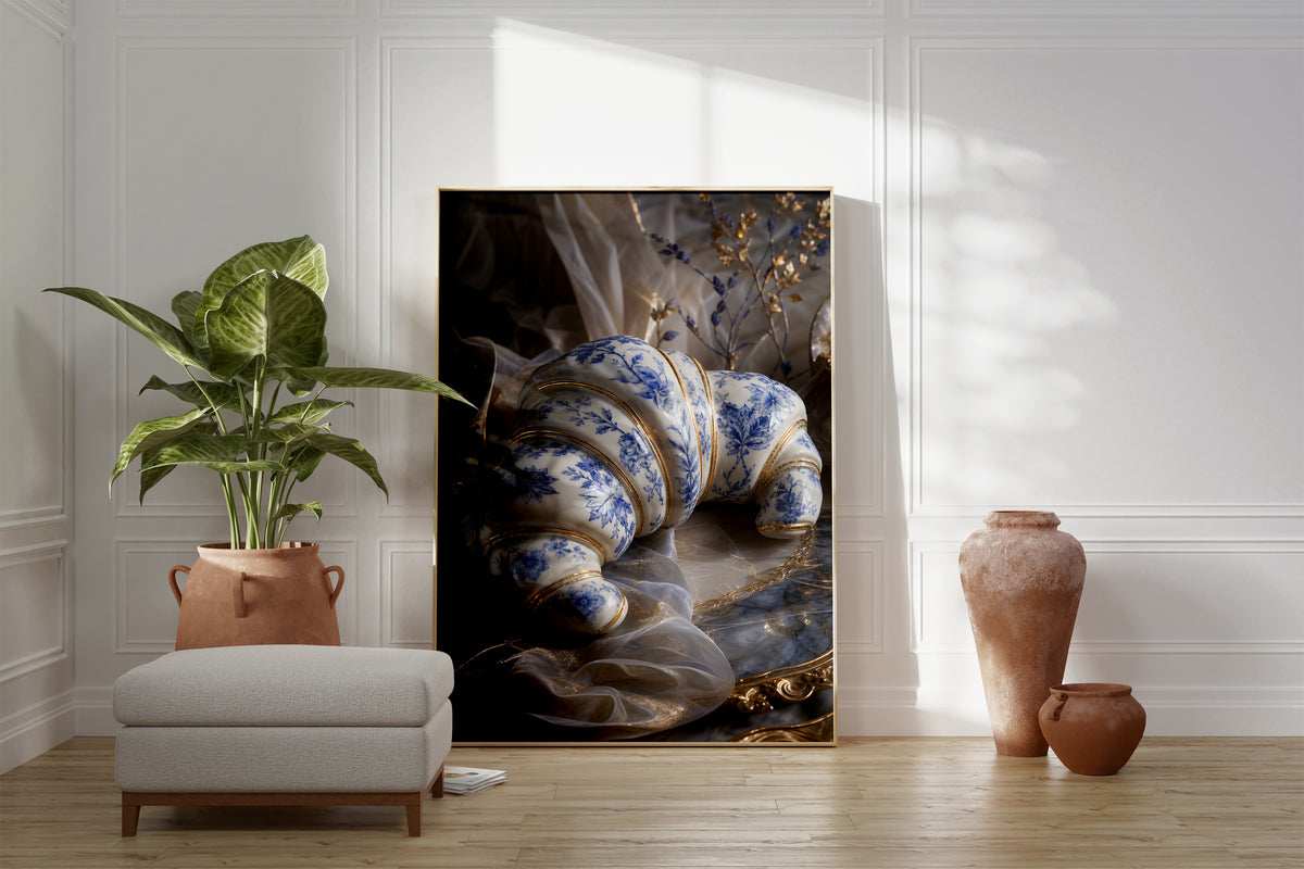 Motiv mit einem weiß-blauen Croissant in Porzellanoptik mit goldenen Verzierungen, als gerahmtes Poster neben Sessel und Zimmerpflanze.