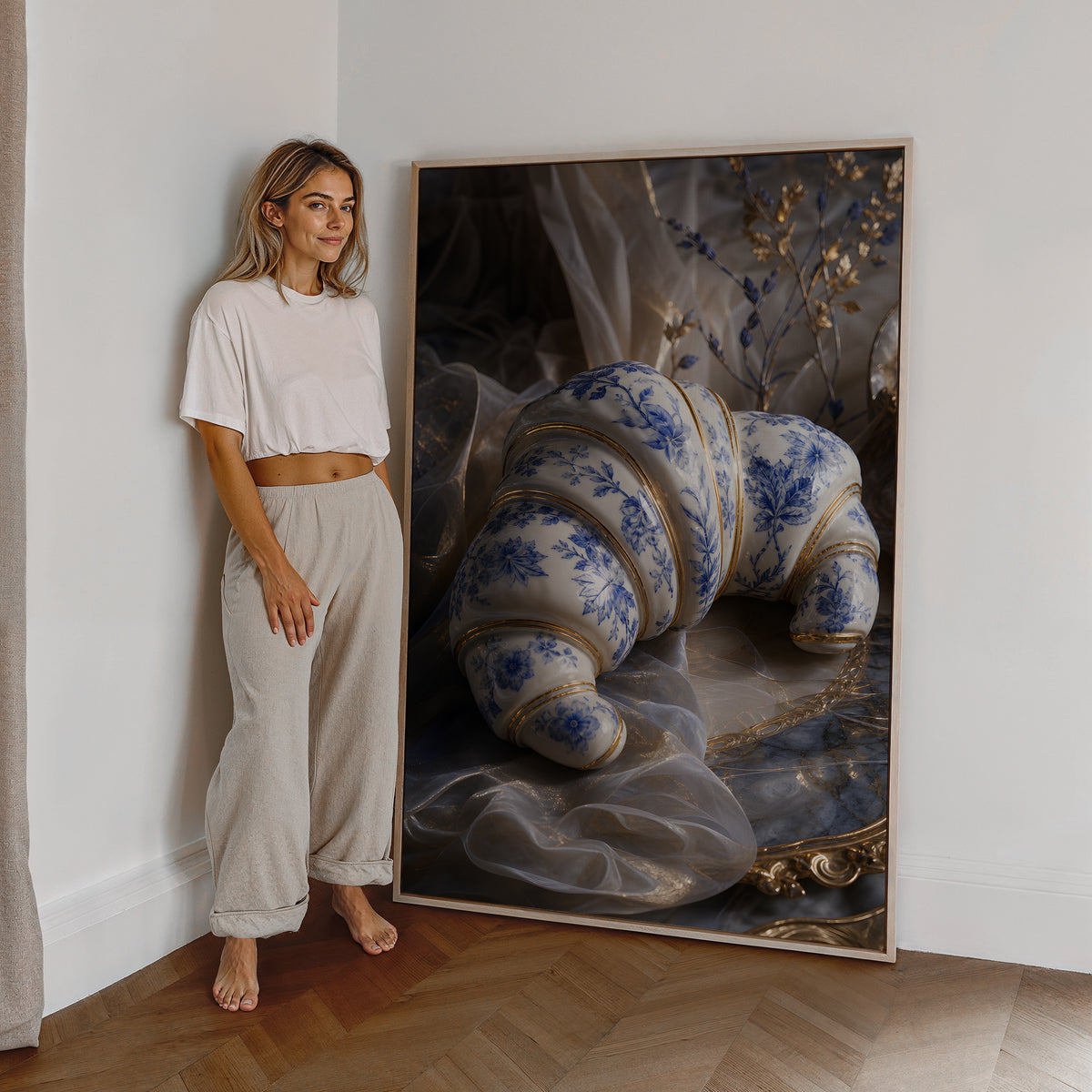 Motiv mit einem weiß-blauen Croissant in Porzellanoptik mit goldenen Verzierungen, als großes gerahmtes Wandbild neben einer Frau.