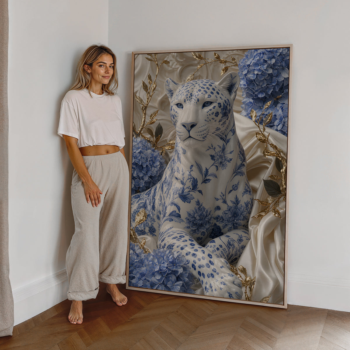 Motiv mit weißem Panther mit blauem Porzellanmuster zwischen Hortensien und goldenen Zweigen, als großes gerahmtes Wandbild neben einer Frau.
