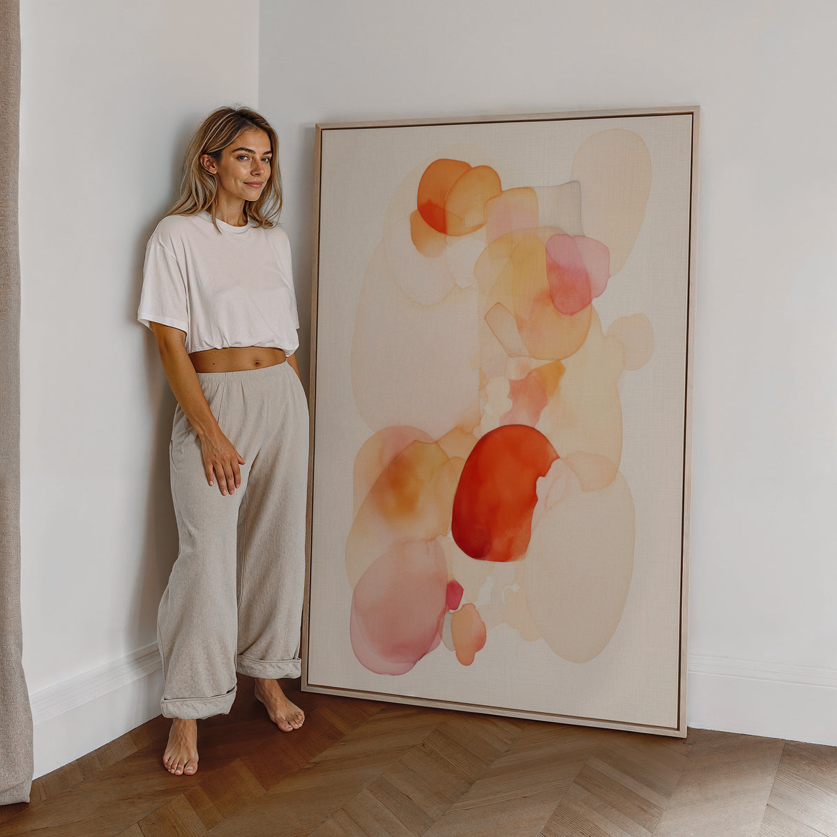 Eine Frau steht neben einem großen gerahmten Poster. Motiv: Transparente abstrakte Farbformen in Orange, Rosa und Creme.