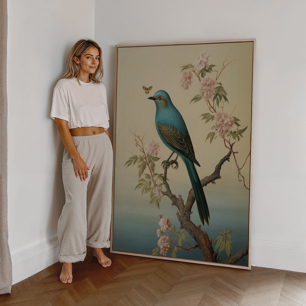 Eine Frau steht neben einem großen gerahmten Poster. Motiv: Blauer Vogel auf einem blühenden Ast vor warmem cremefarbenem Hintergrund.