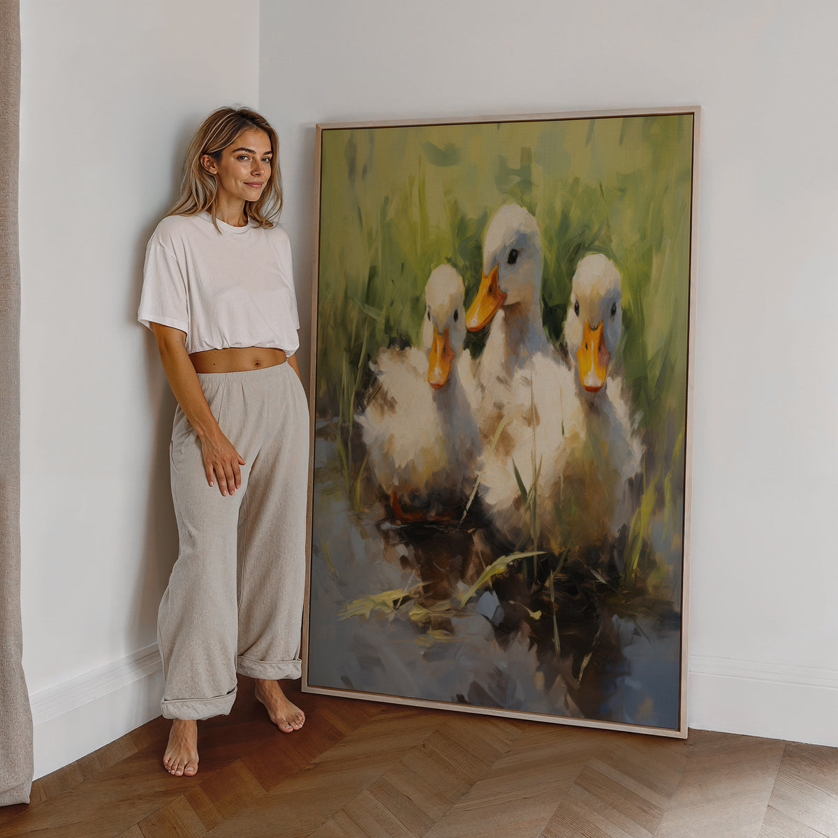 Eine Frau steht neben einem großen gerahmten Poster. Motiv: Drei helle Entenküken mit orangefarbenen Schnäbeln am Wasser.