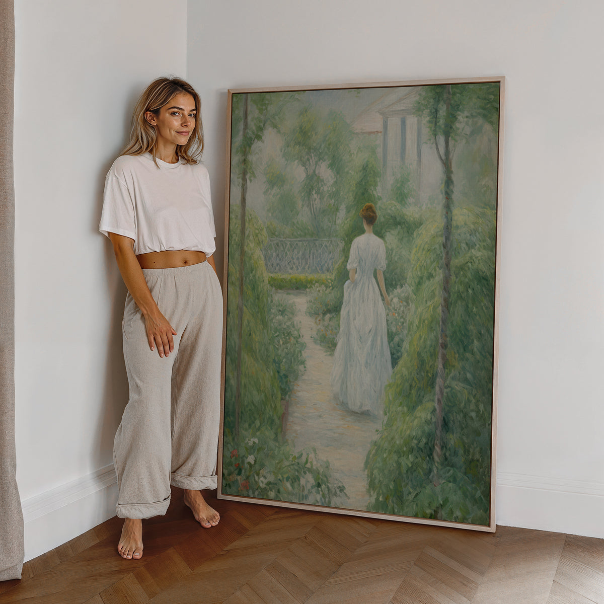 Eine Frau steht neben einem großen gerahmten Poster. Motiv: Frau im weißen Kleid auf einem von Pflanzen umgebenen Gartenweg.