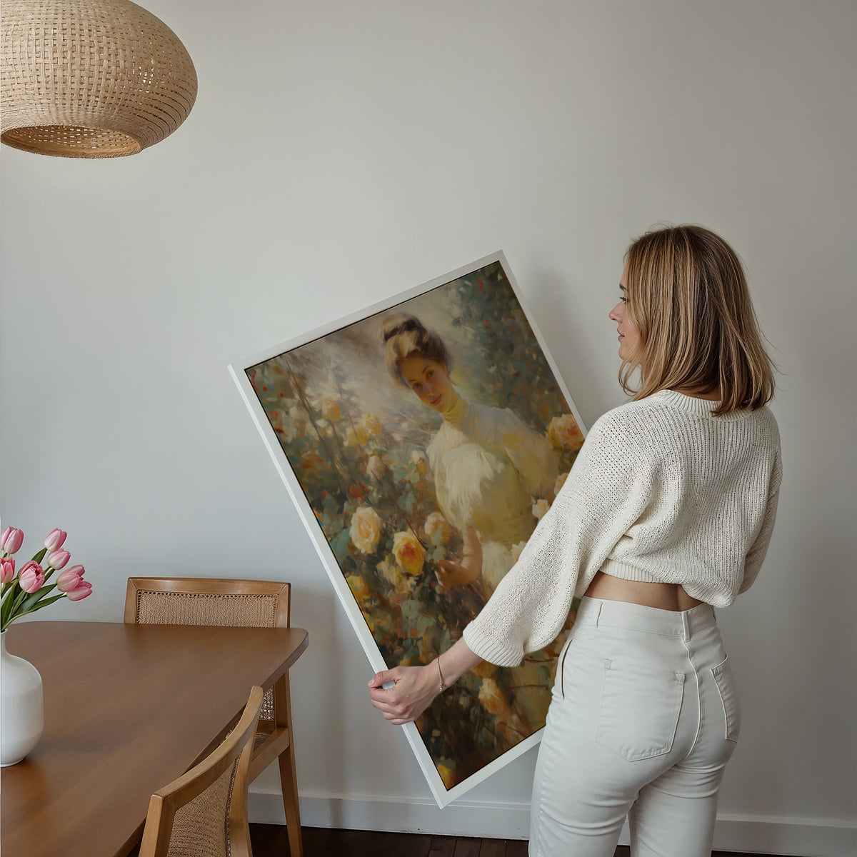 Eine Frau hält ein großes gerahmtes Poster im Essbereich mit Holzmöbeln. Motiv: Frau im hellen Kleid umgeben von gelben Rosen.