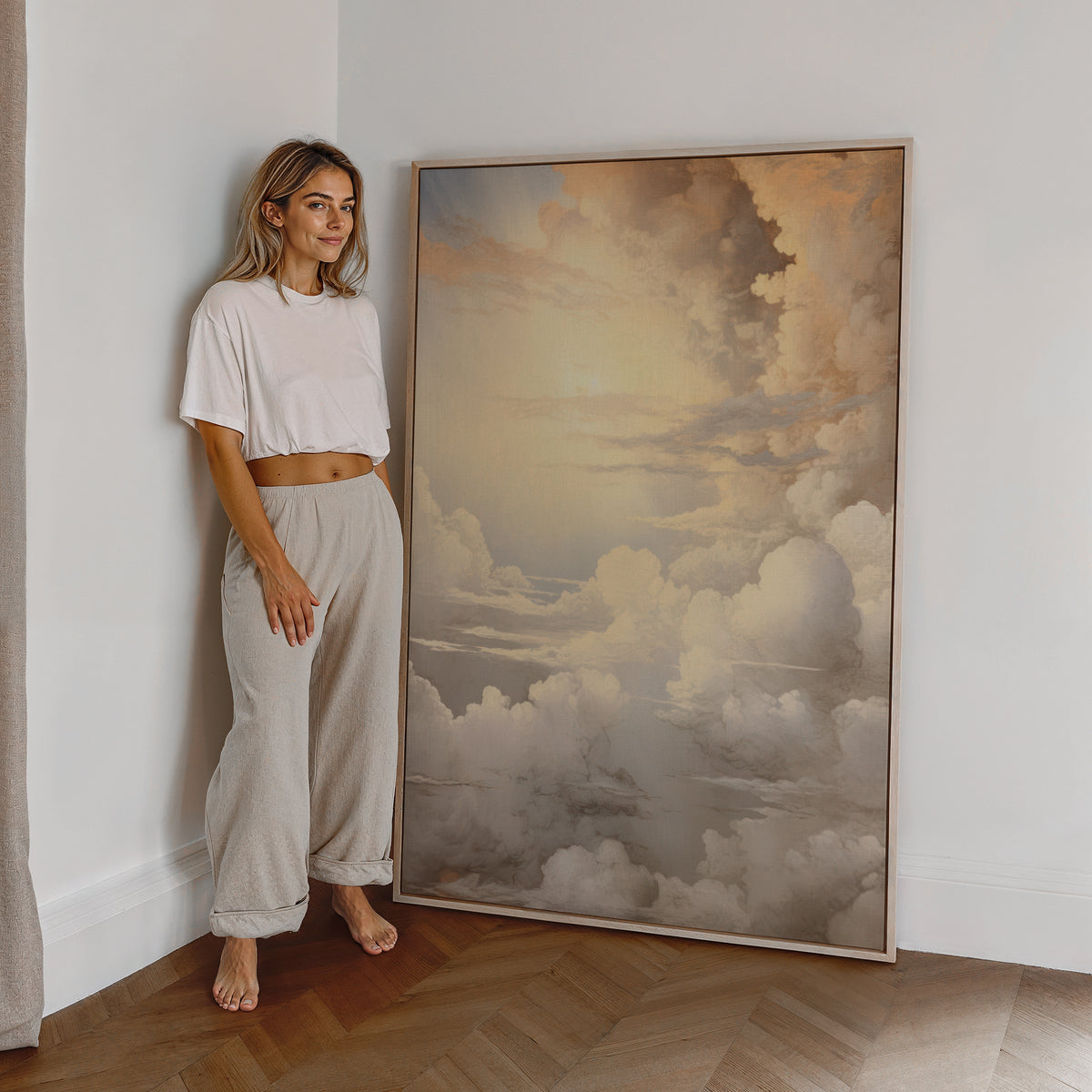 Eine Frau steht neben einem großen gerahmten Poster. Motiv: Weiche Wolken in Creme und Gold mit hellem Himmel.