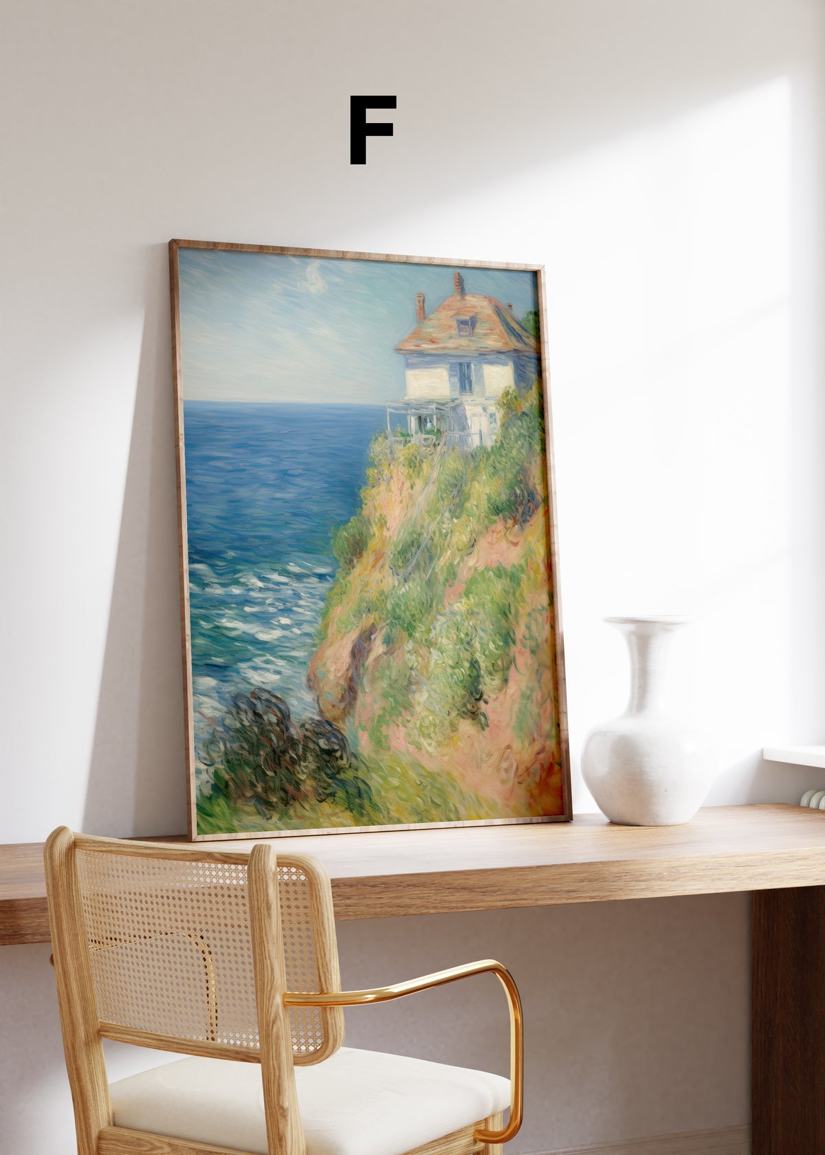 Postermotiv F: Helles Haus an einer begrünten Steilküste über dem blauen Meer. Im Holzrahmen auf einem Schreibtisch.