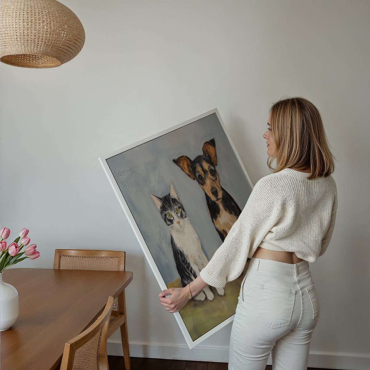 Eine Frau hält ein großes gerahmtes Poster im Essbereich mit Holzmöbeln. Motiv: Eine kleine Katze und ein brauner Hund nebeneinander vor einem graublauen Hintergrund.