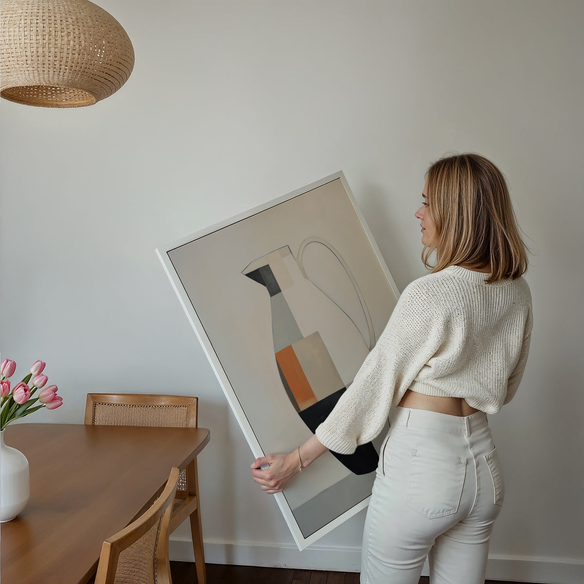Eine Frau hält ein großes gerahmtes Poster im Essbereich mit Holzmöbeln. Motiv: Geometrisch gestalteter Krug in Schwarz, Creme, Grau und Orange.