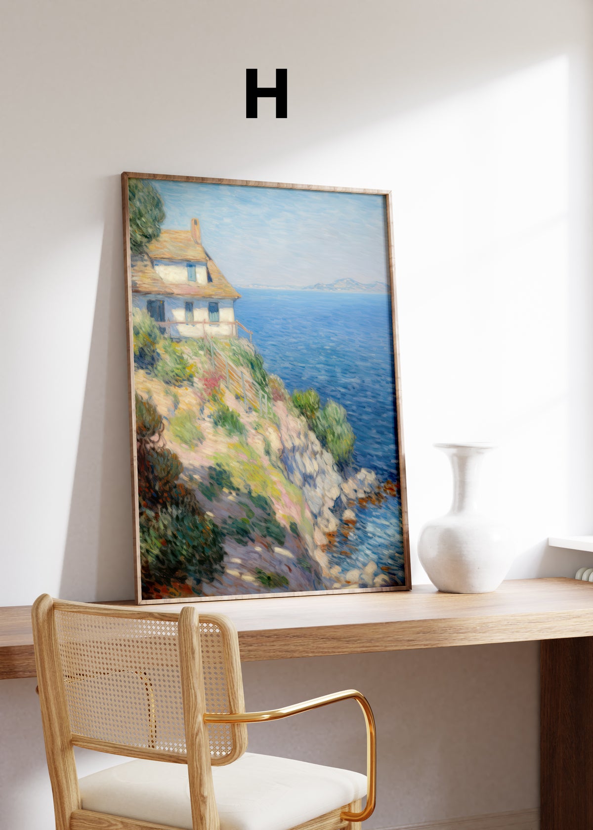 Postermotiv H: Helles Haus auf einer felsigen Küste über dem blauen Meer. Im Holzrahmen auf einem Schreibtisch.